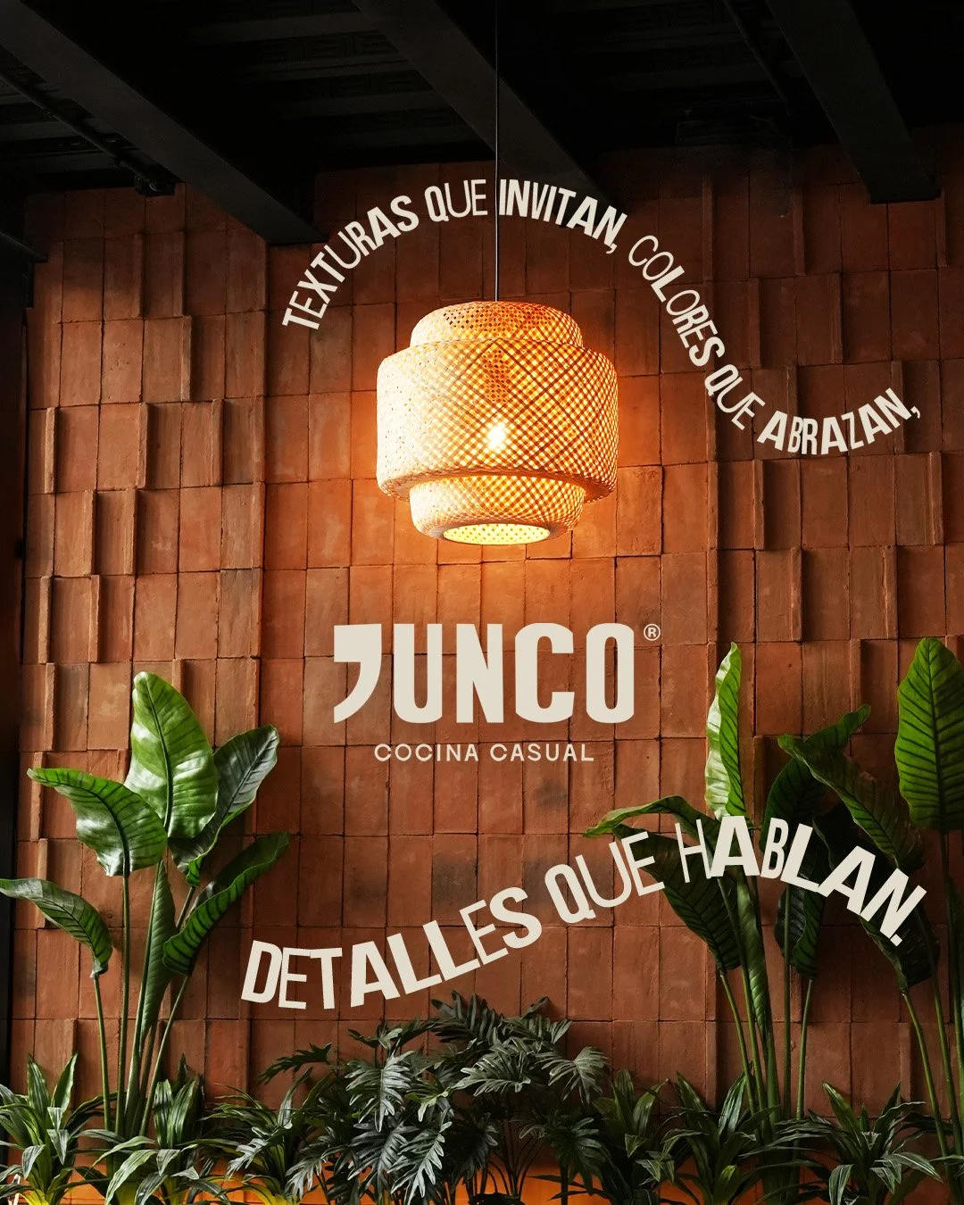 Pared de madera decorada con plantas verdes y una lámpara colgante de mimbre, con texto en español que dice 'Texturas que invitan, colores que abrazan', 'Junco, cocina casual', y 'Detalles que hablan'.