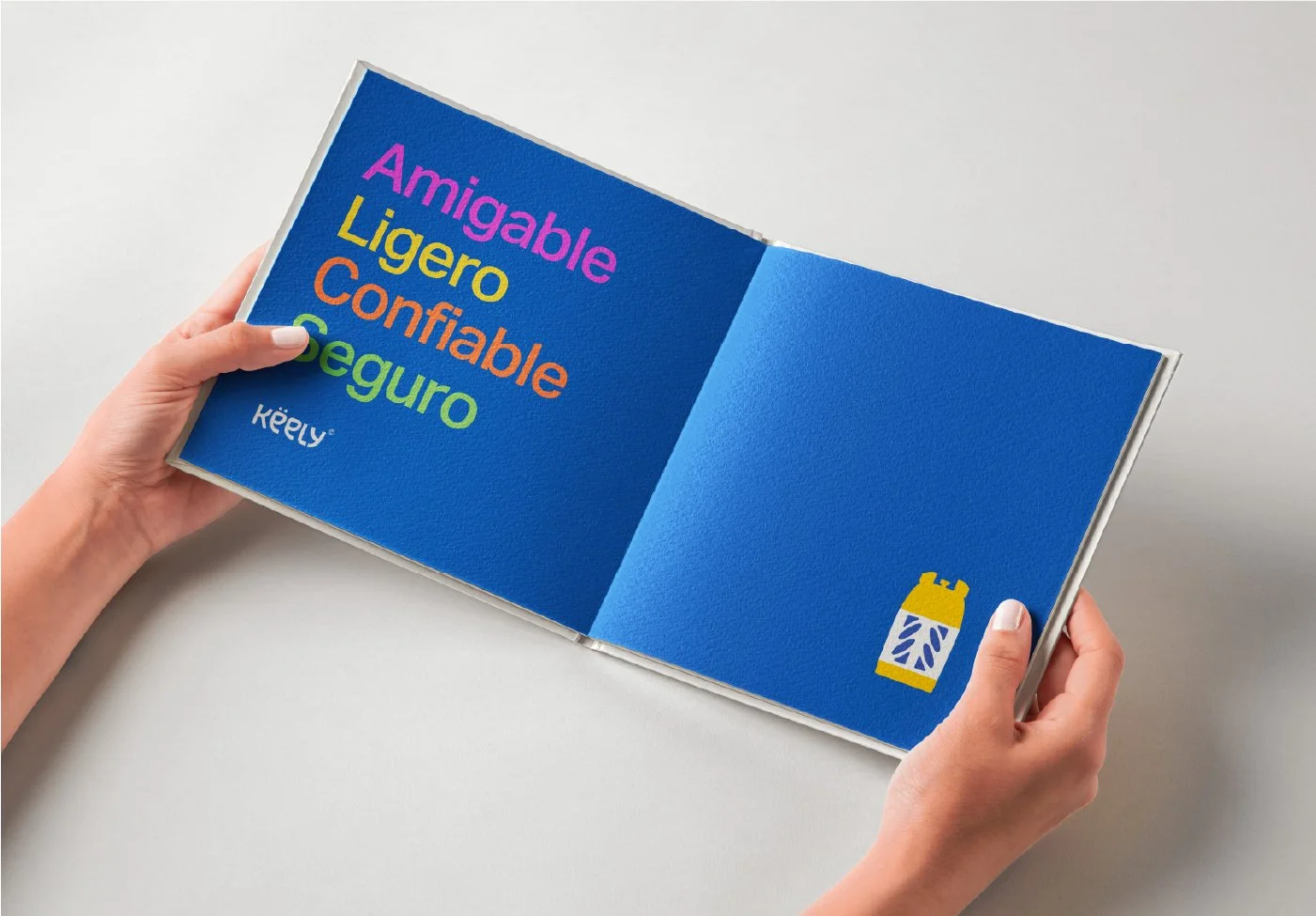 Manos sosteniendo un libro con fondo azul, que tiene palabras en diferentes colores y un dibujo de una botella en la página derecha.