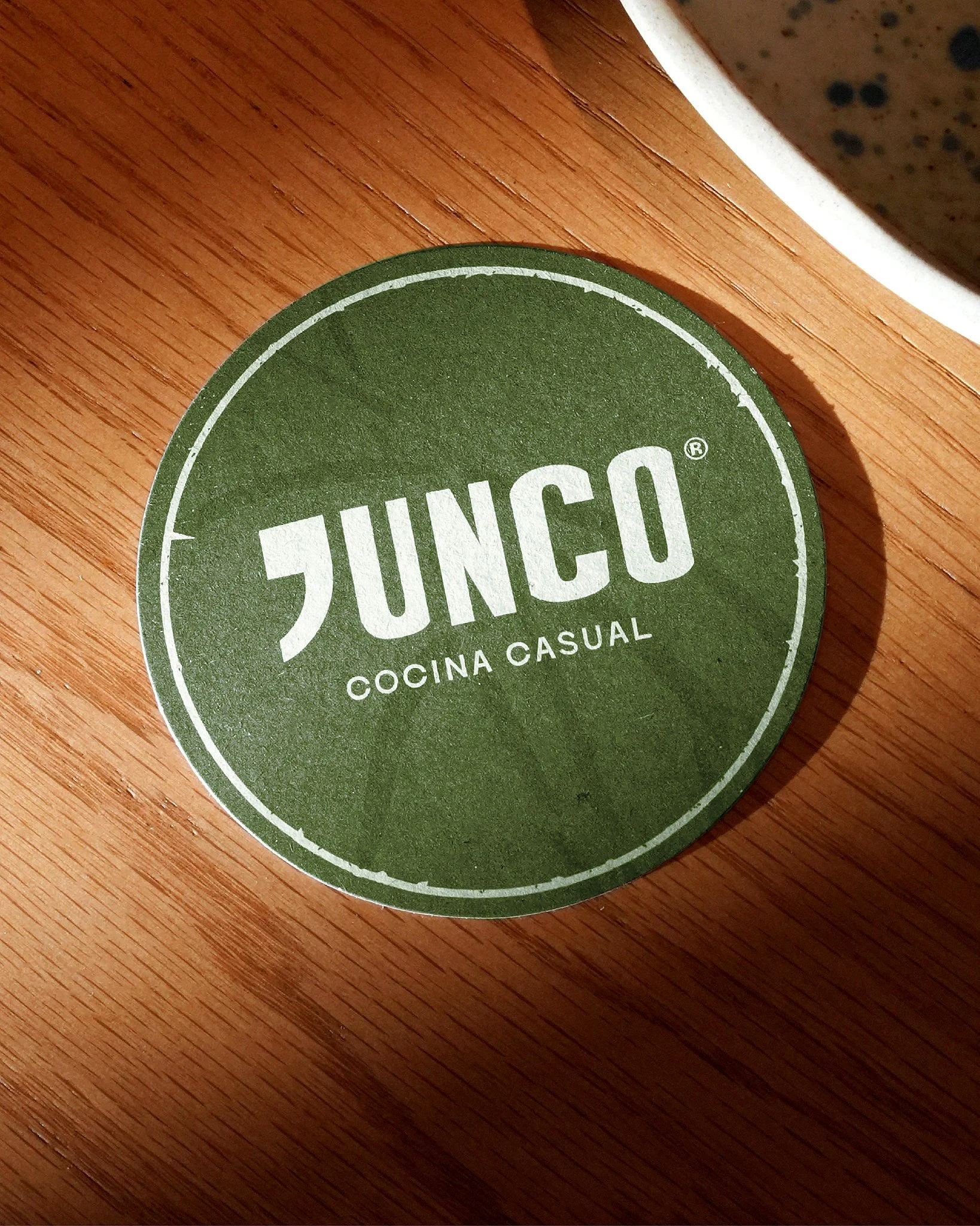Etiqueta circular verde en una superficie de madera con las palabras 'JUNCO' y 'Cocina Casual' en letras blancas.