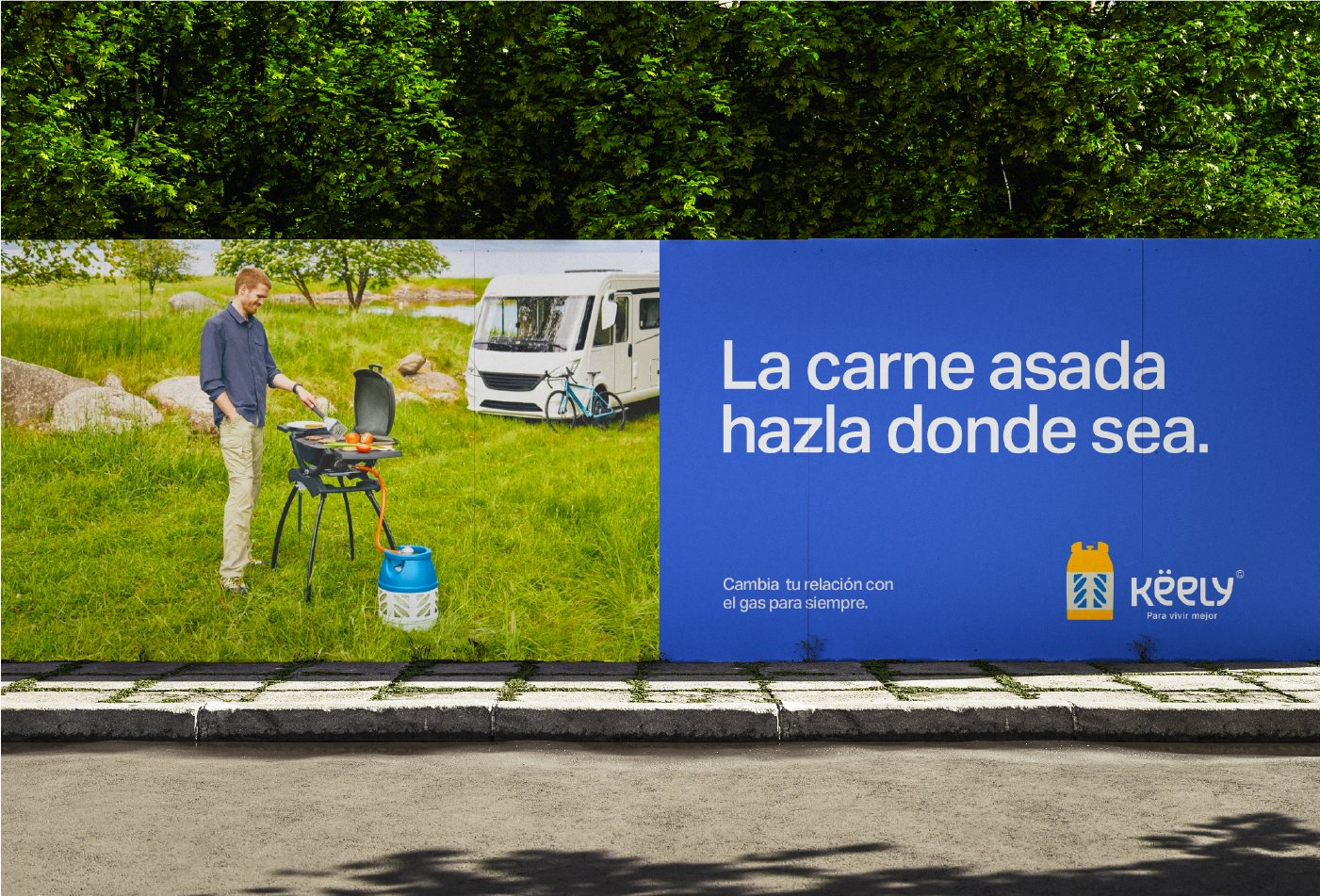 Cartel publicitario que muestra a un hombre cocinando en una parrilla portátil en un campo y un área de camping con caravanas y bicicleta. Texto en español que dice "La carne asada hazla donde sea" y un logotipo un mensaje de promover el uso de gas para cocinar.