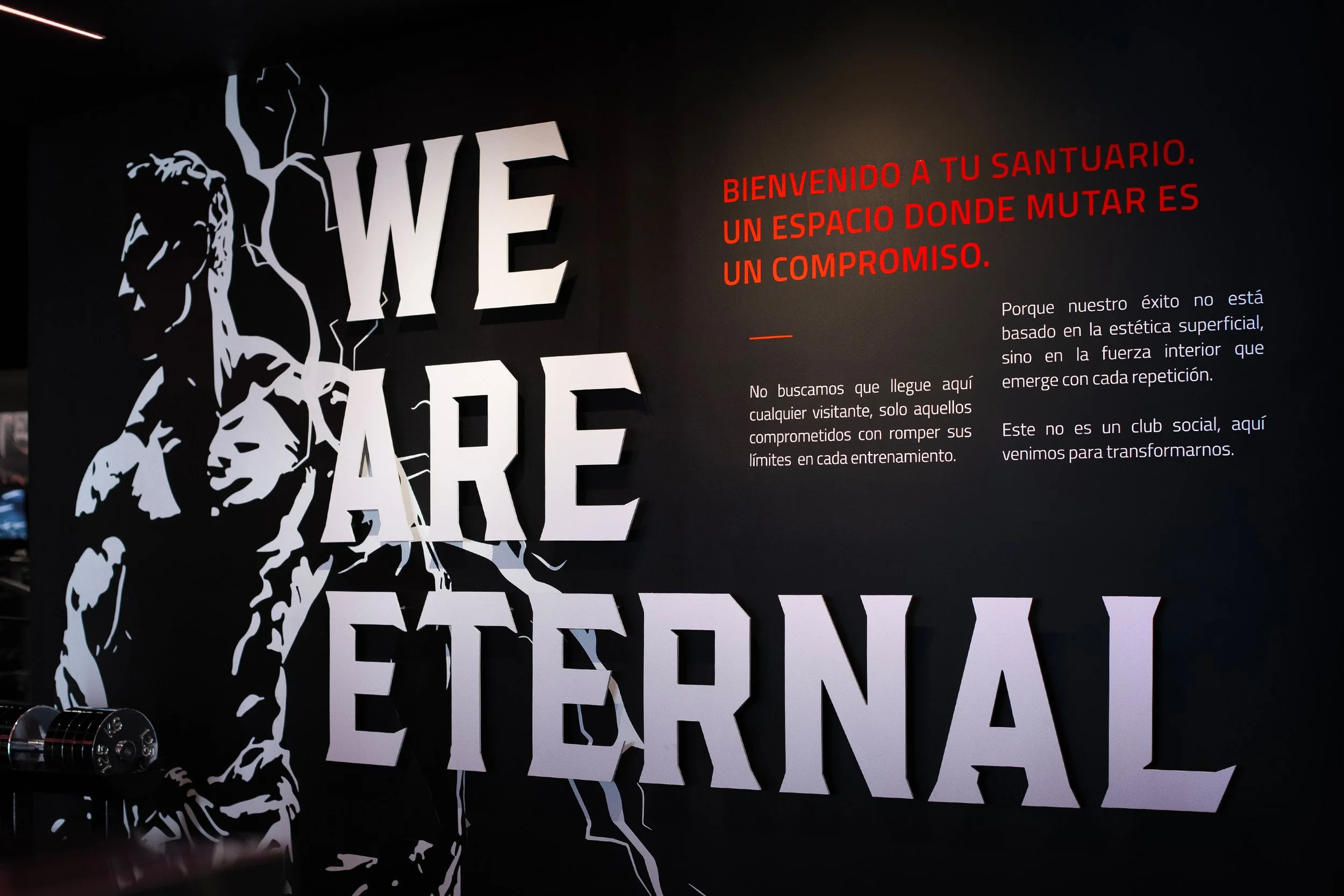 Pared con letras grandes que dicen 'WE ARE ETERNAL' y un dibujo de una persona en estilo de línea, junto a un texto en español en color rojo y blanco que da la bienvenida y explica el propósito del espacio.