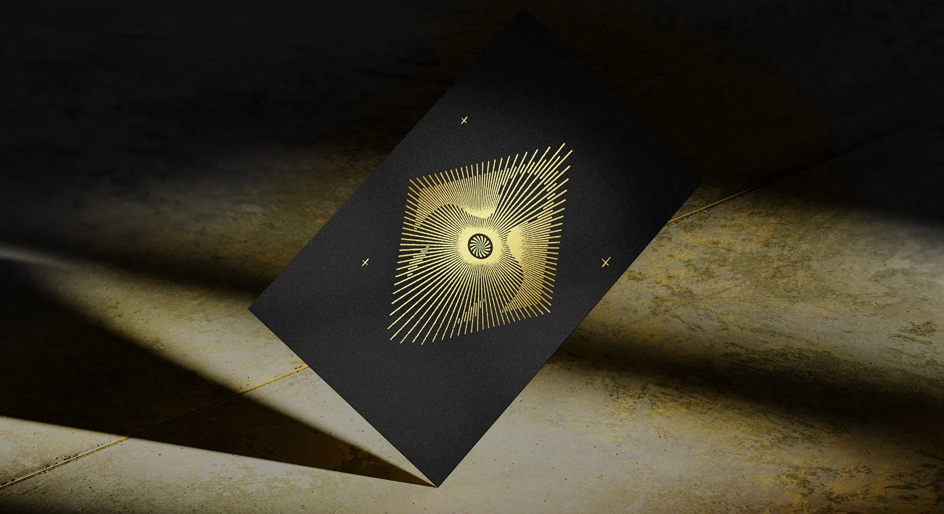 Tarjeta negra con diseño dorado que presenta un patrón geométrico y líneas radiantes, colocada sobre una superficie de piedra.
