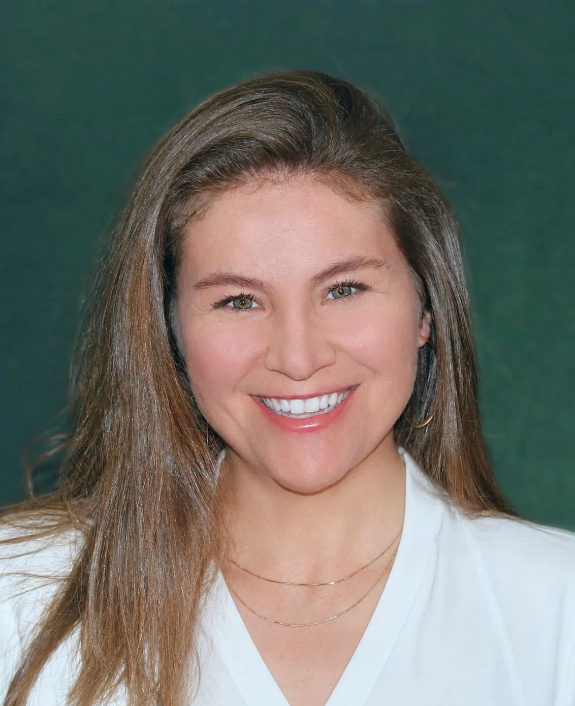 A woman with long wavy brown hair smiling, wearing a denim jacket and a green top.