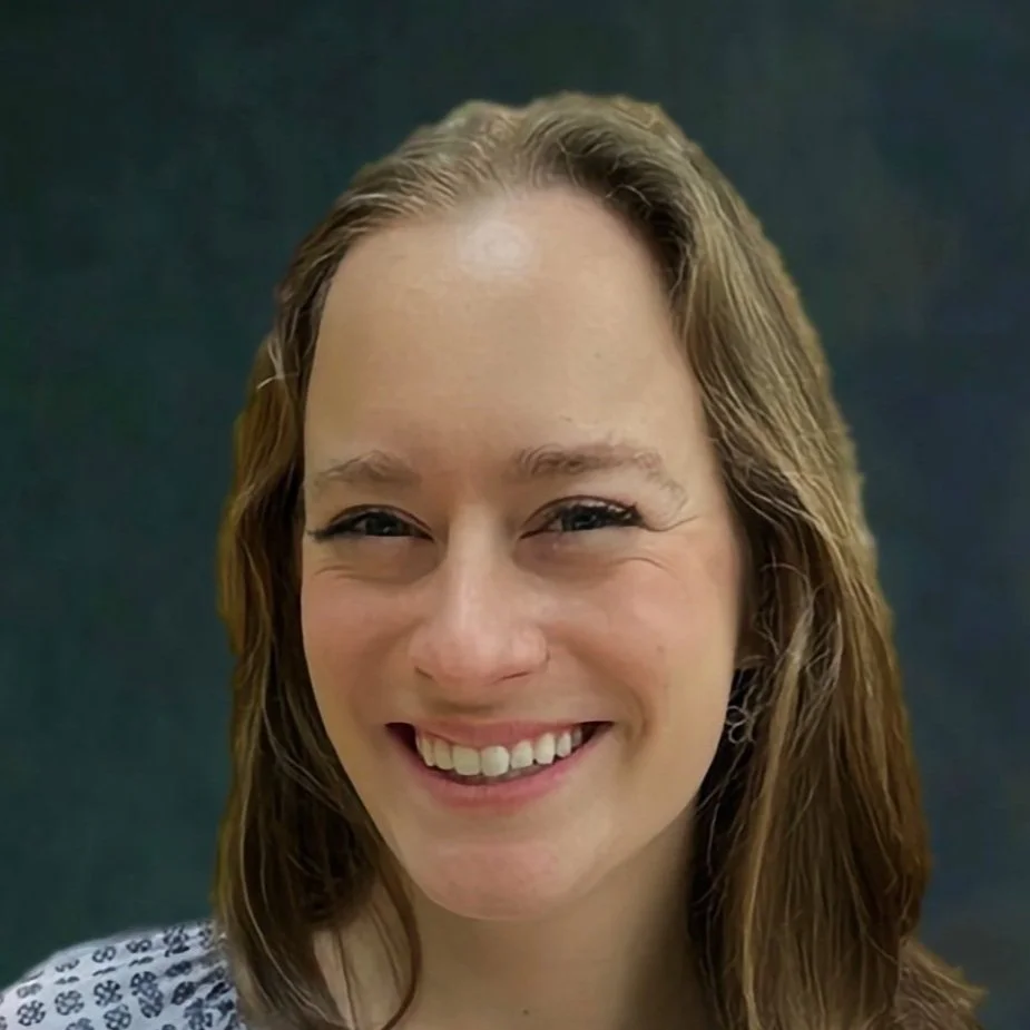 Close-up of a woman with shoulder-length wavy hair smiling against a dark background.
