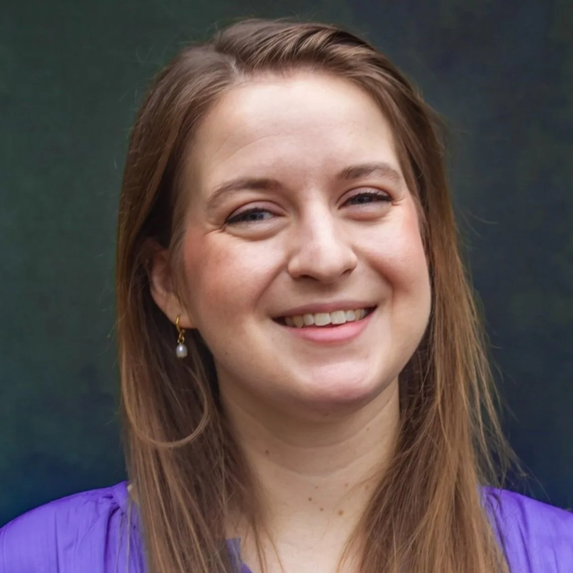 A woman with light brown hair, wearing earrings, smiling, against a dark green background.
