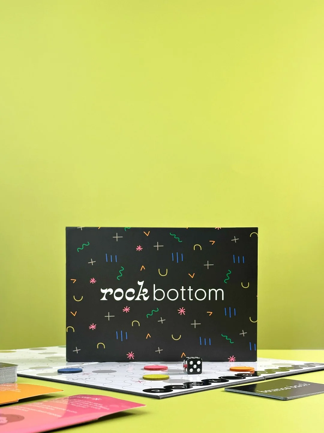 Rock Bottom box sitting on top of the game board with tokens, a die, character cards, and bounce back cards surrounding it.