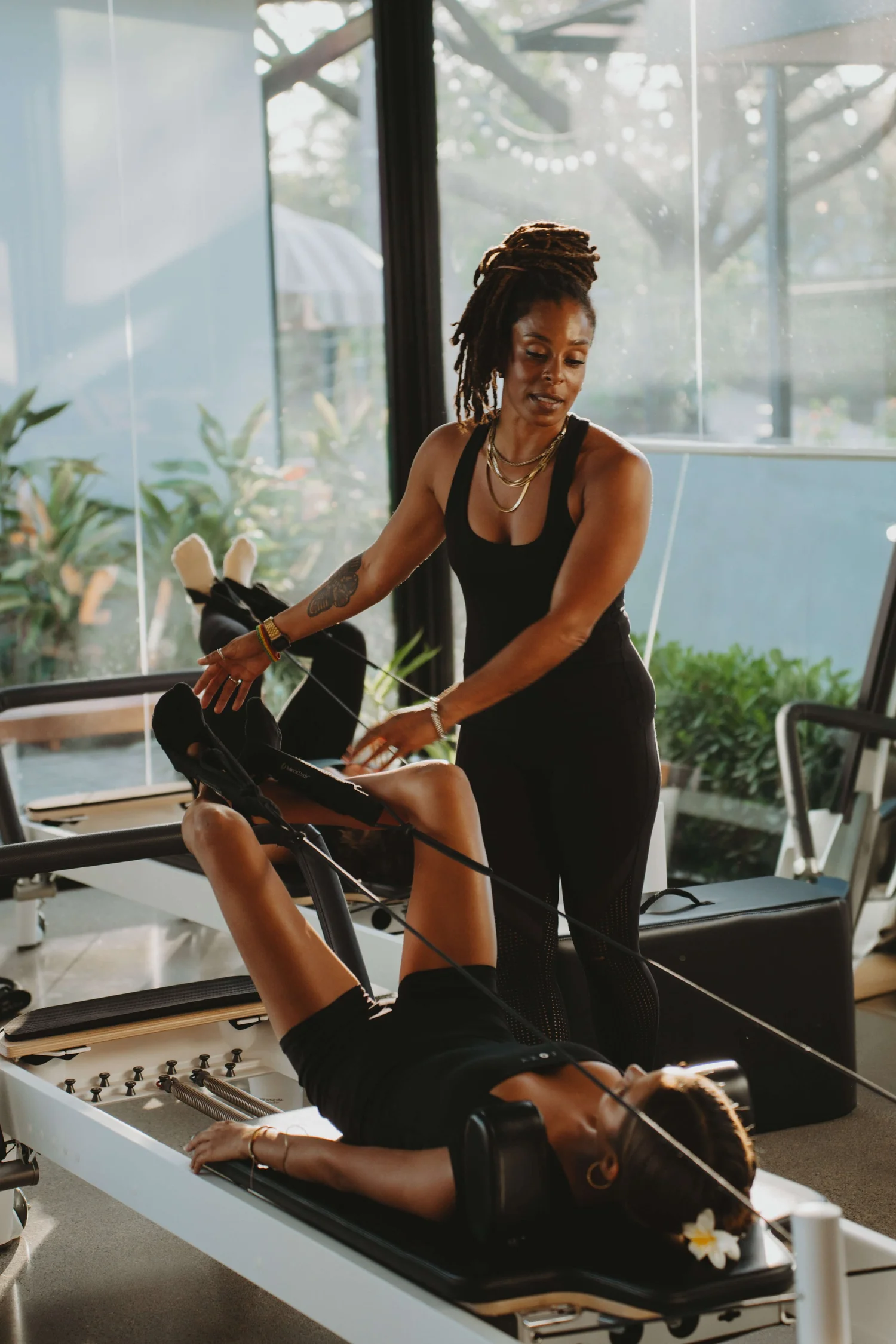 A woman doing Pilates on a reformer machine with an instructor nearby