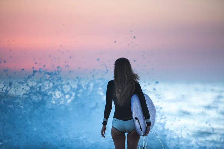 Surfer heading into the waves at Playa Guiones, Nosara — Black Cat Studio Pilates retreat