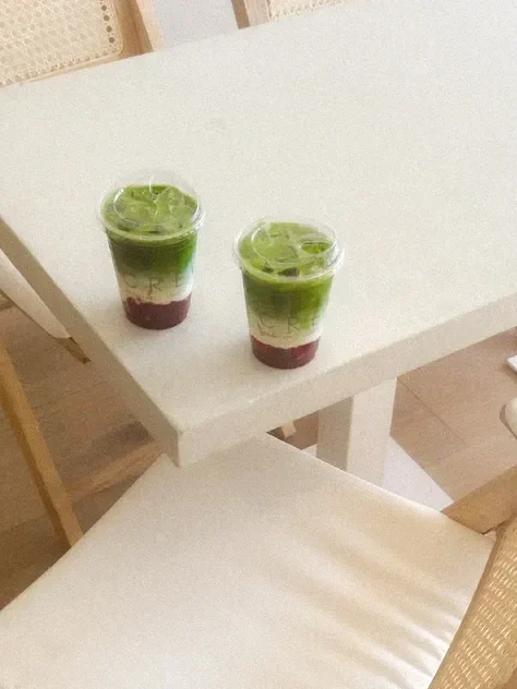 Two clear plastic cups filled with green layered drinks, garnished with lime slices on top, placed on a white table.
