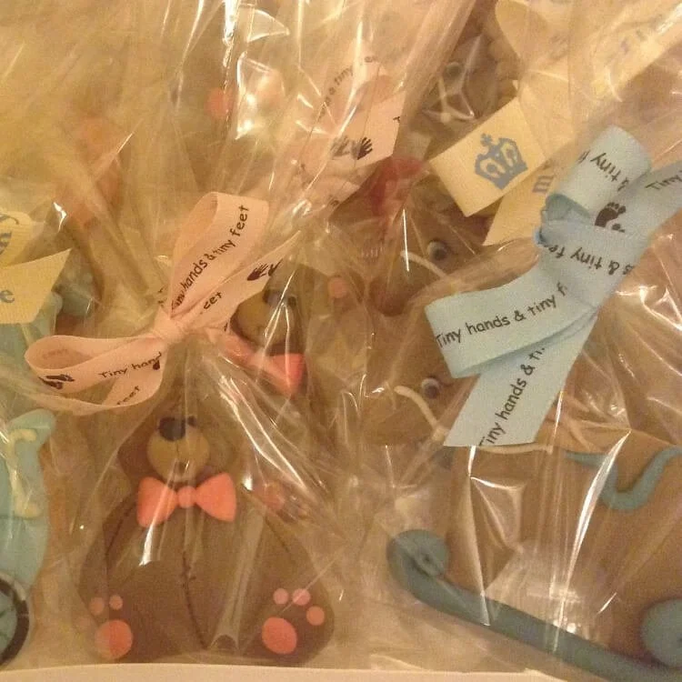 Chocolate teddy bear-shaped cookies wrapped in cellophane with pink and blue ribbons for a baby shower.