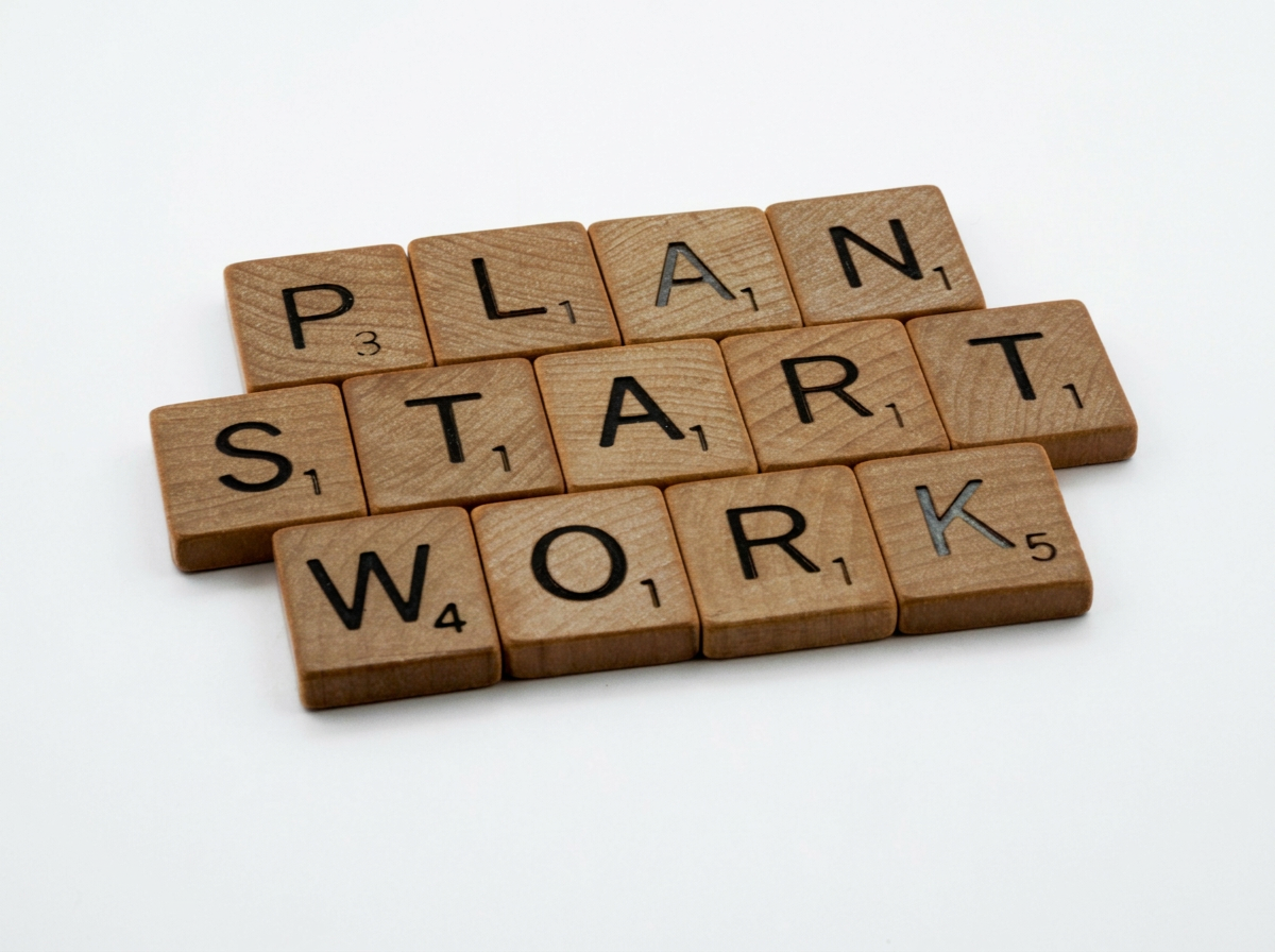 Wooden Scrabble tiles spelling out 'PLAN', 'START', and 'WORK' on a white background.