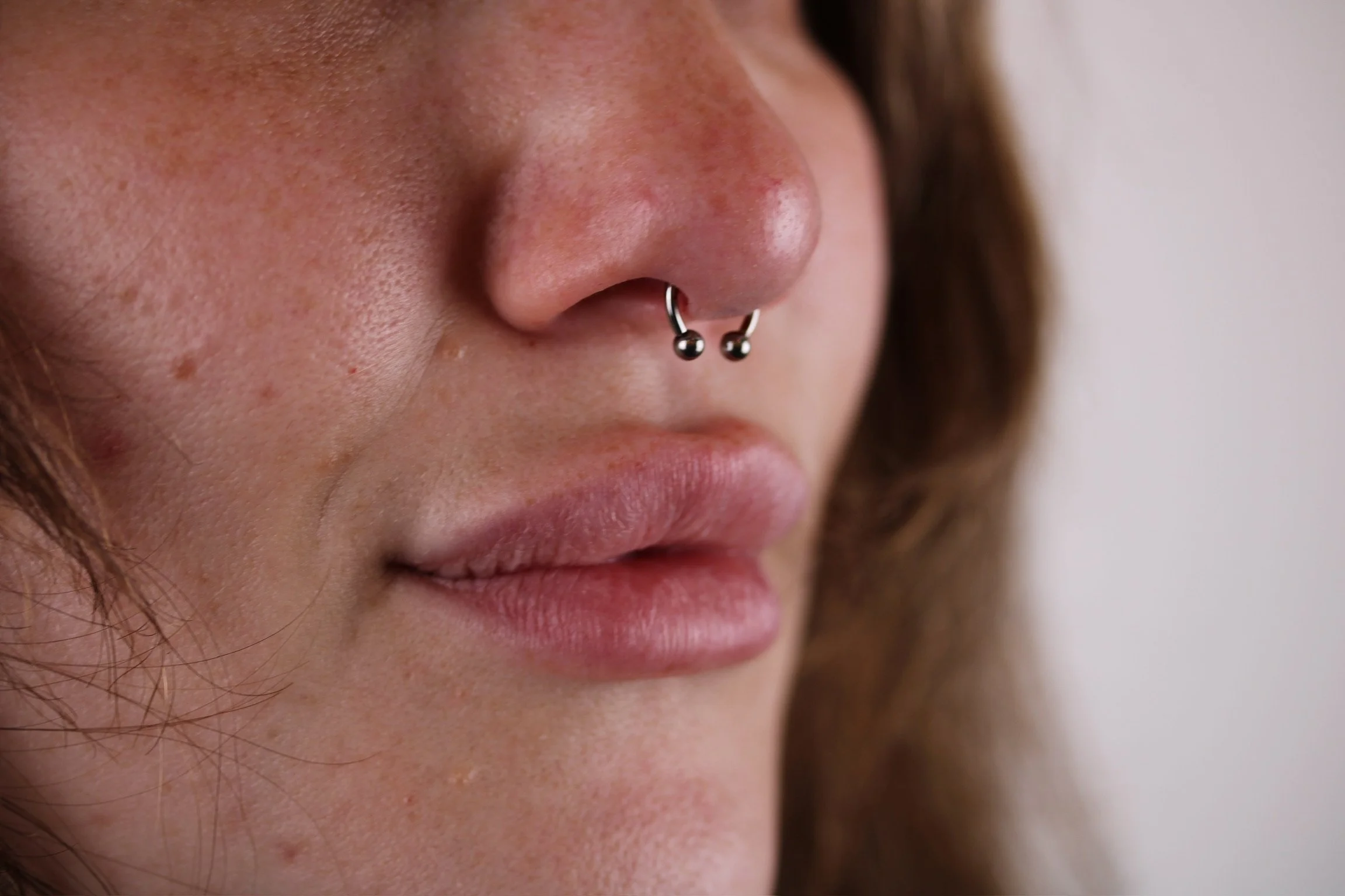 Close-up of a person's face showing a nose with a septum piercing and lips.