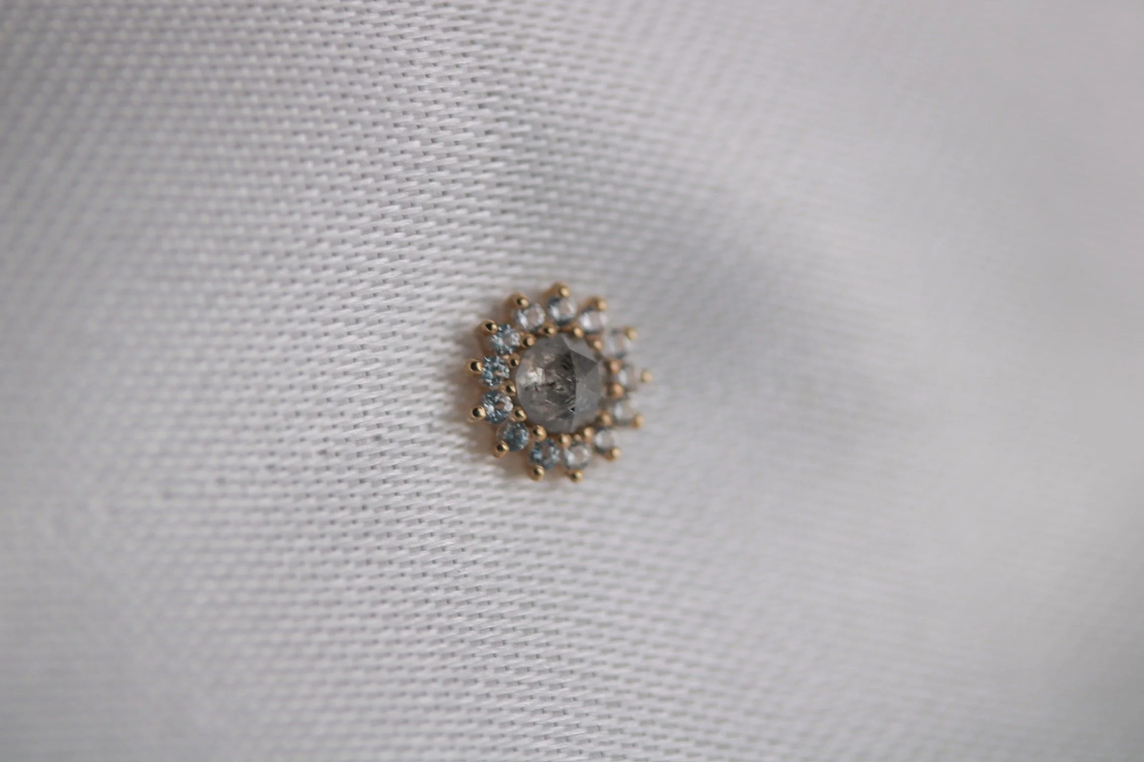 Close-up of a decorative brooch with a central gemstone surrounded by smaller clear stones, attached to white fabric.