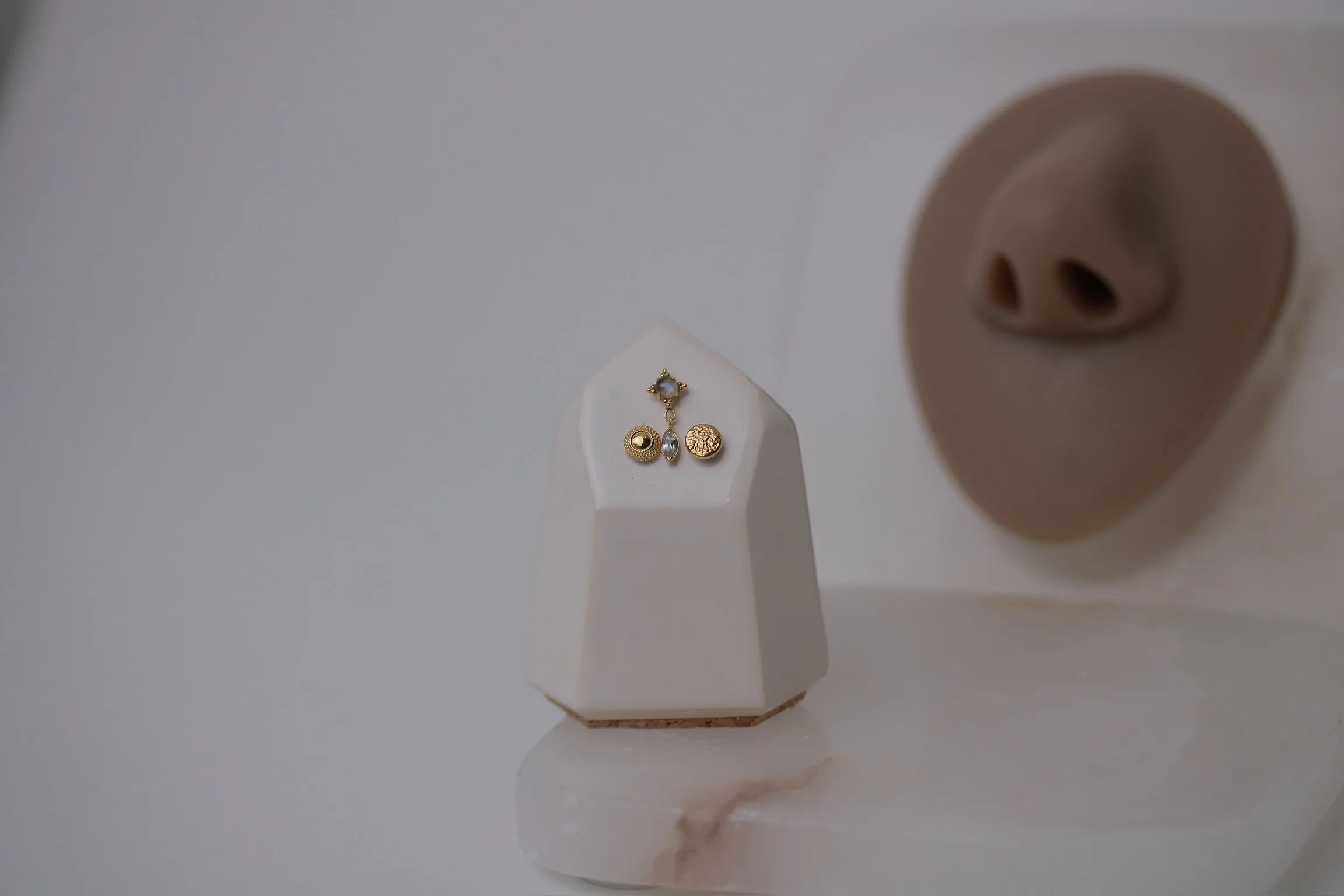 Close-up of gold jewelry pieces displayed on a white geometric stand, with a partial view of a bear-shaped sculpture in the background.