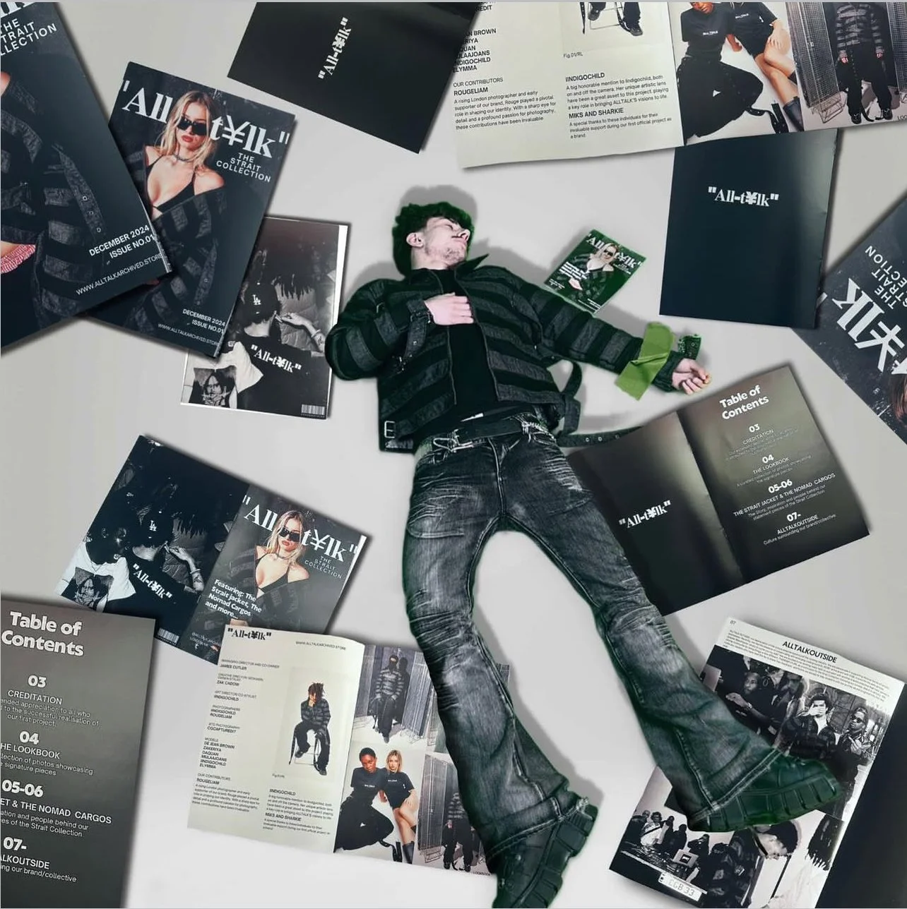 A young man lying on the floor surrounded by magazines and brochures for All-tëk, a fashion brand. He wears a black jacket, distressed jeans, and black boots.
