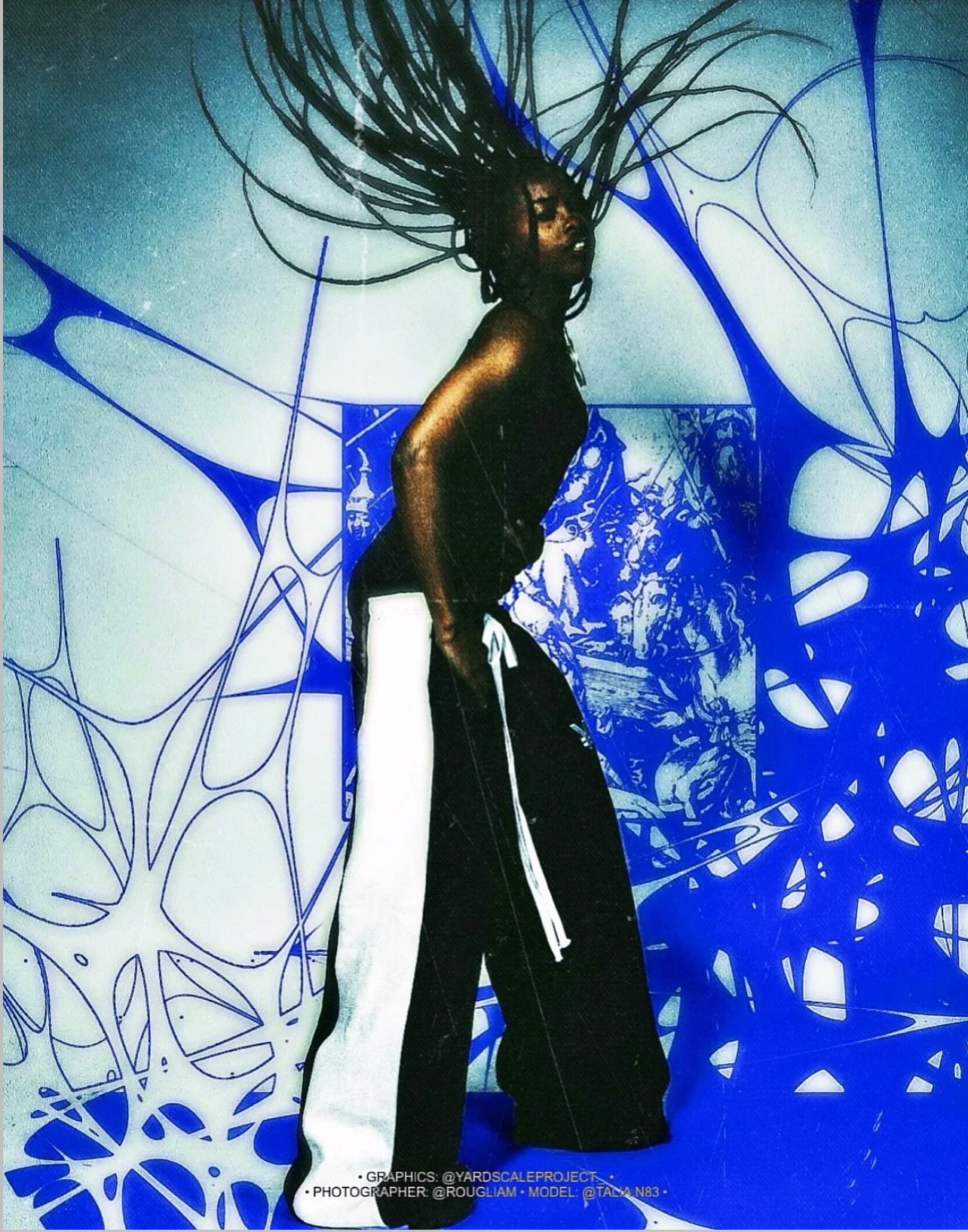 A woman with dreadlocks, wearing a black top and black pants with a white side stripe, standing in front of a blue and white patterned background.