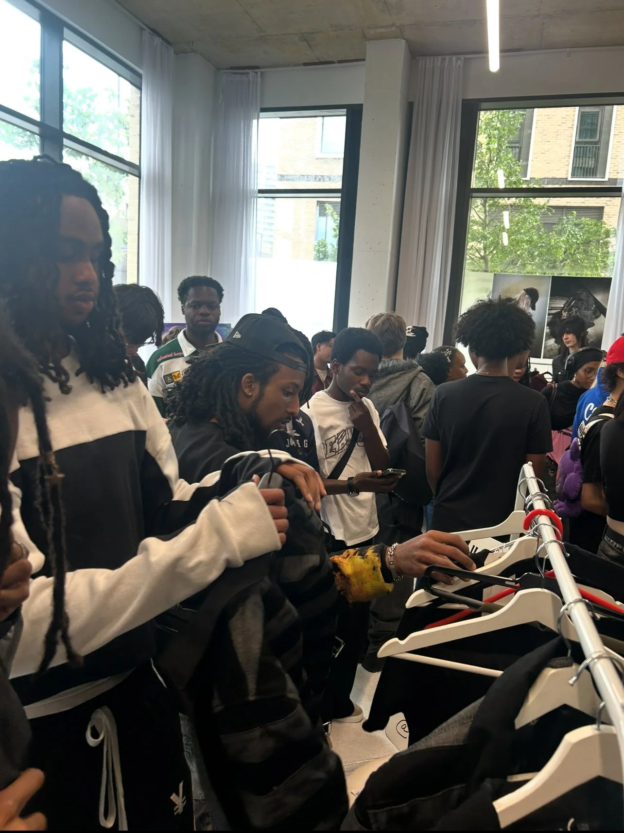 A group of people shopping at a clothing store, browsing and examining clothes on racks.