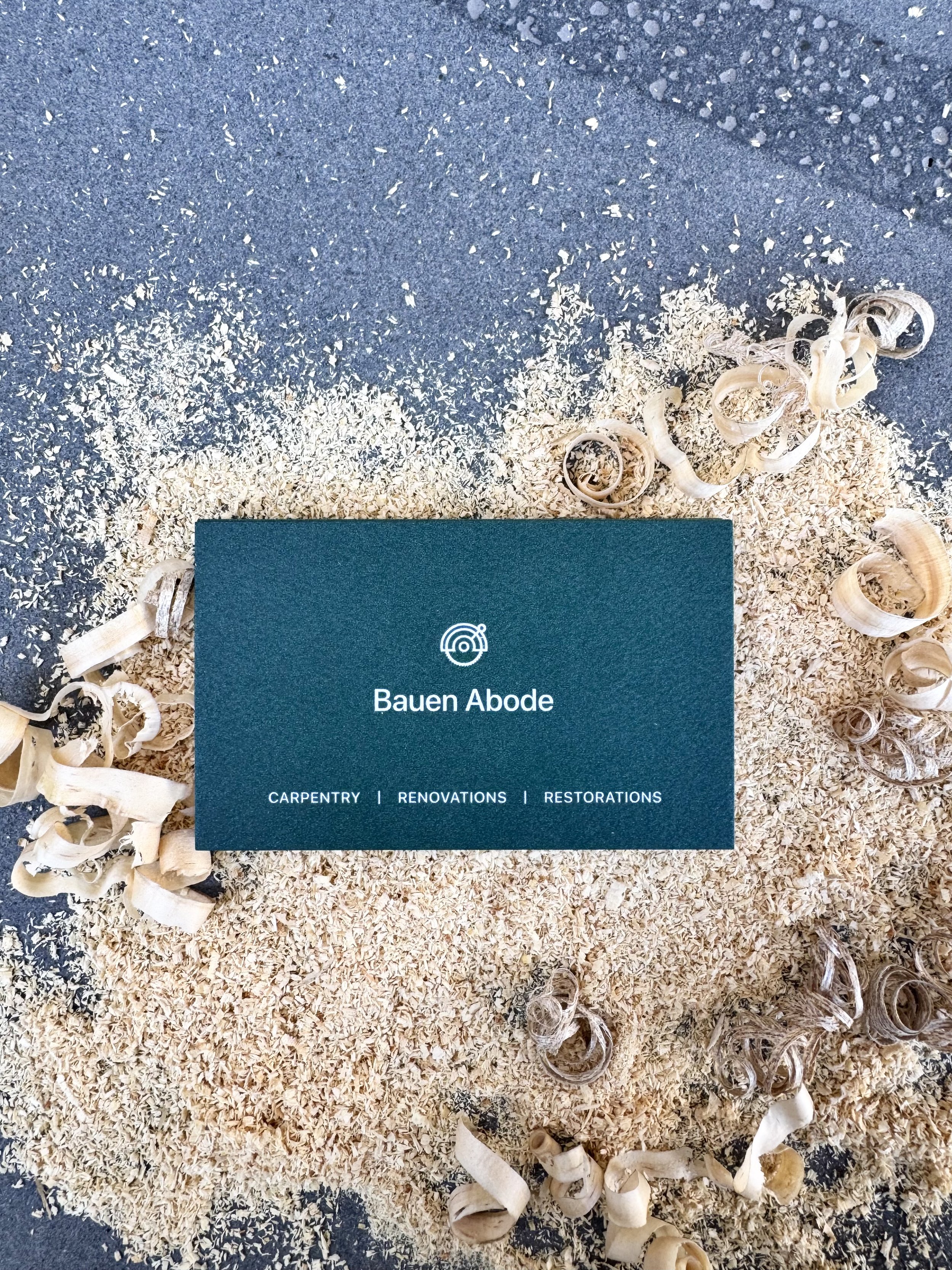 Business card for Bauen Abode on a bed of wood shavings with wood curls around it.