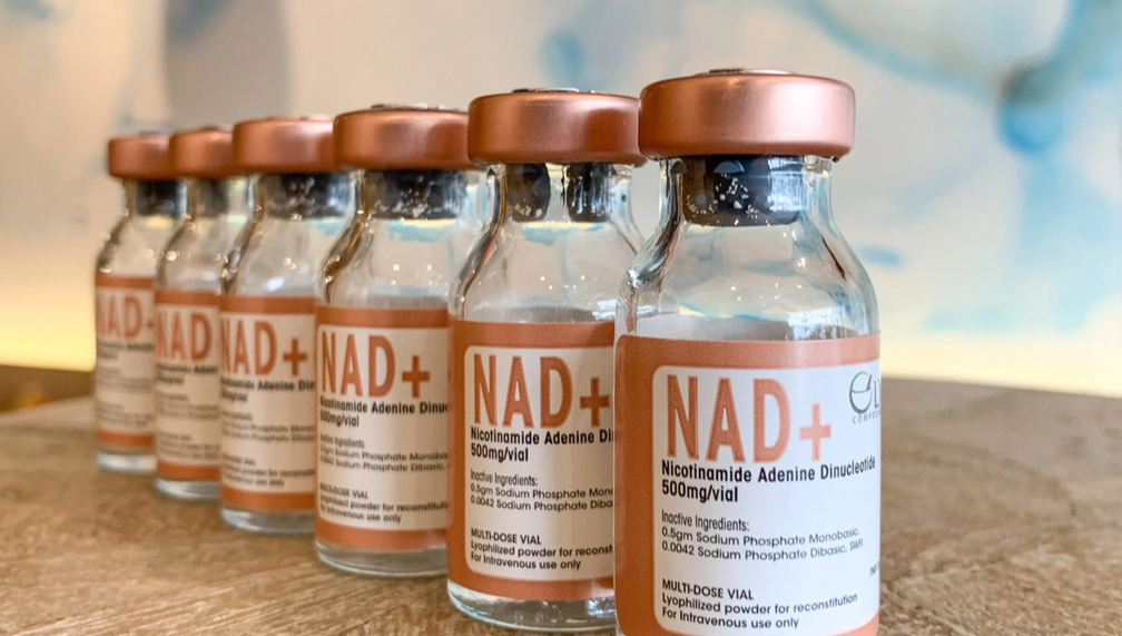 Six glass vials labeled 'NAD+' with orange caps, arranged in a row on a wooden surface, used for medical or scientific purposes.