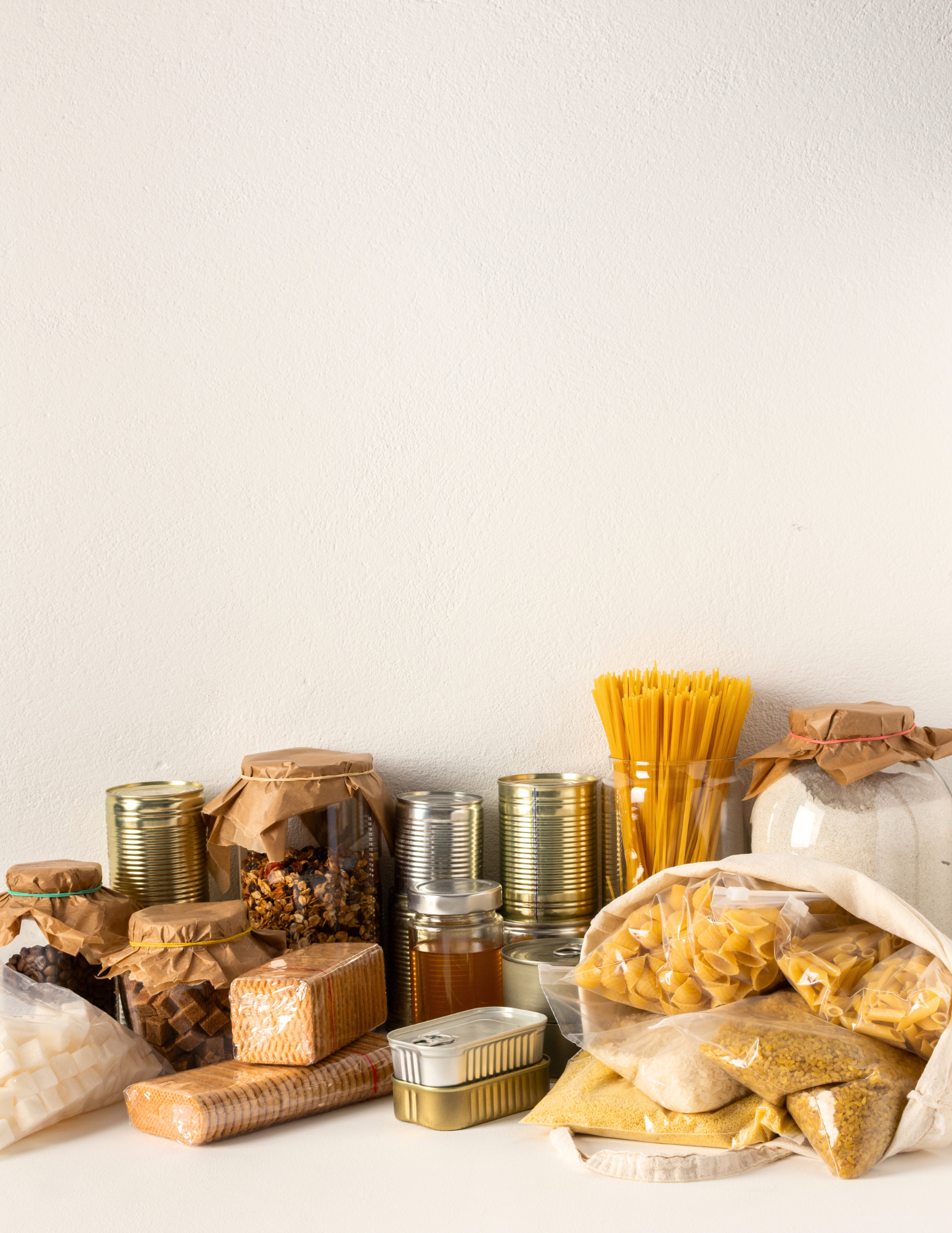 An assortment of food items displayed on a white background, including dry pasta, canned goods, and packaged snacks.