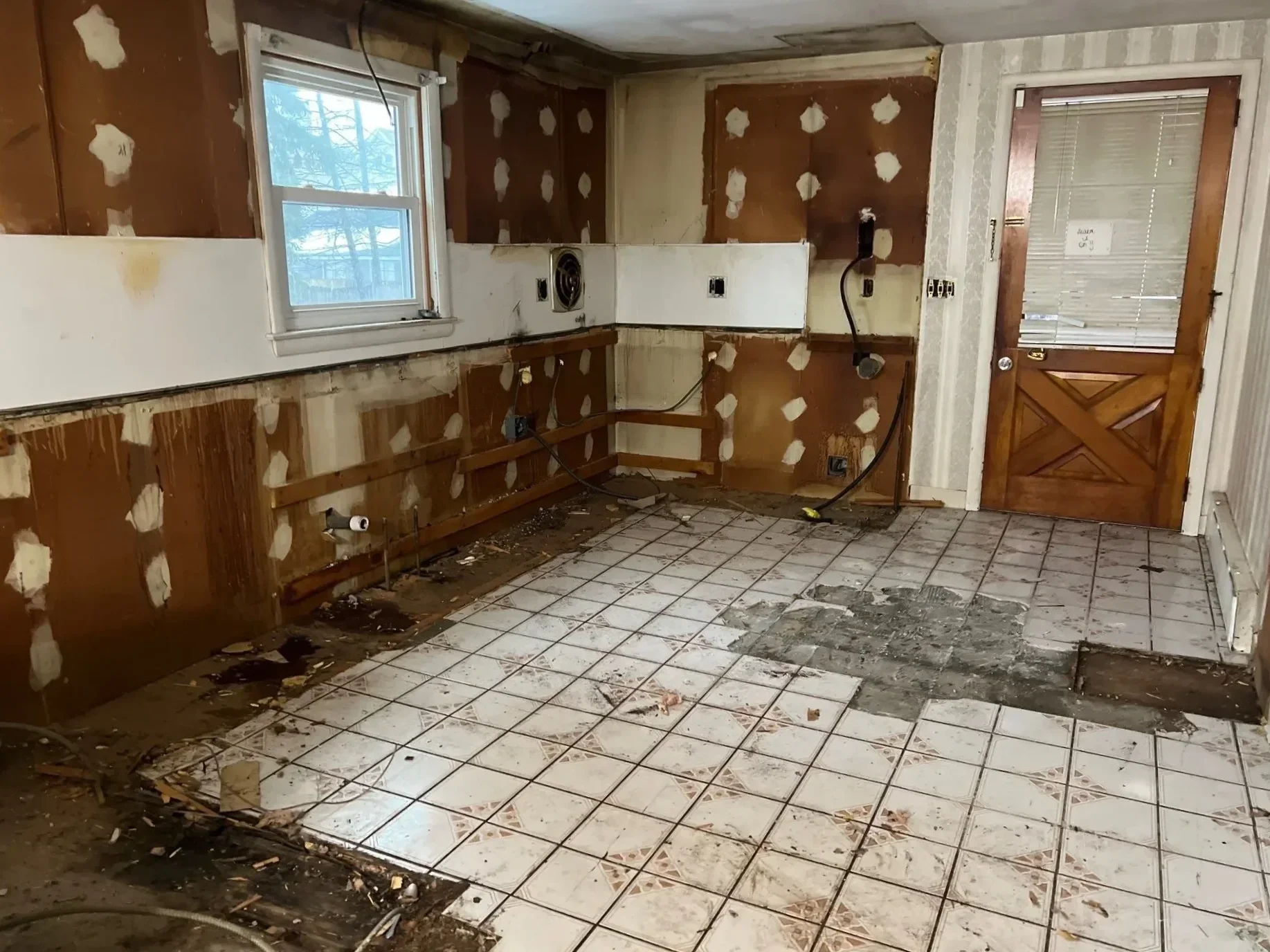 Kitchen before remodel showing full demolition with stripped walls and old tile flooring in Connecticut