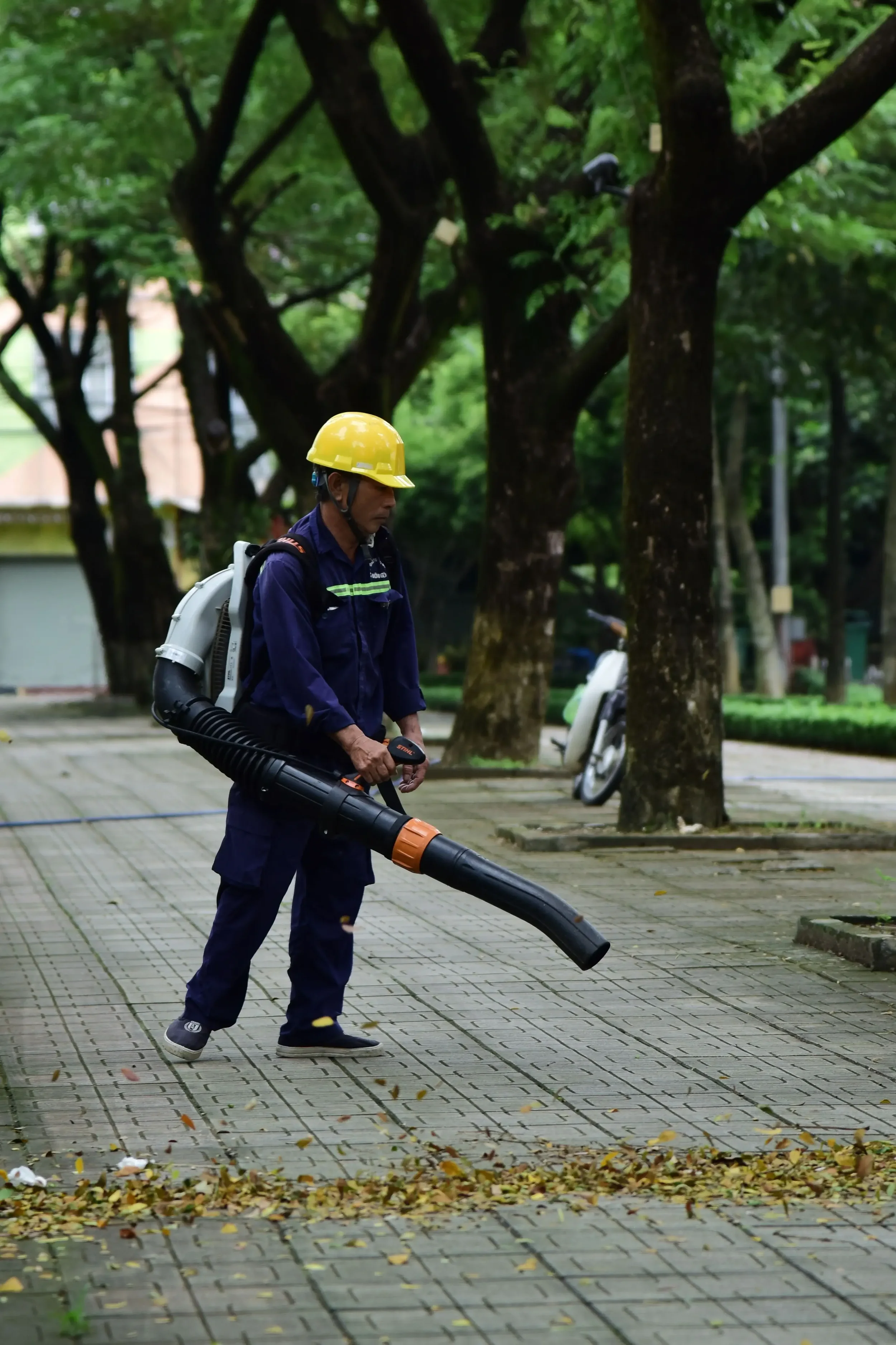 Grounds crew technician using a backpack leaf blower to clear a commercial walkway during fall cleanup in Connecticut