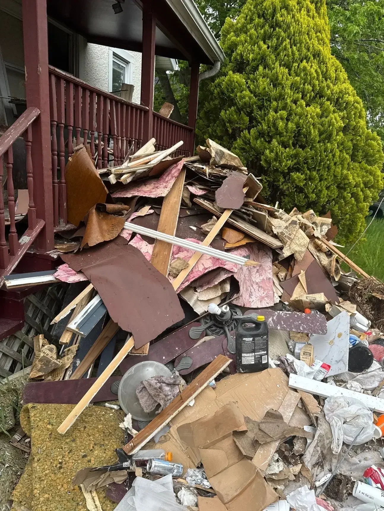 Construction debris, lumber, and household items piled on a porch during a foreclosure cleanout.