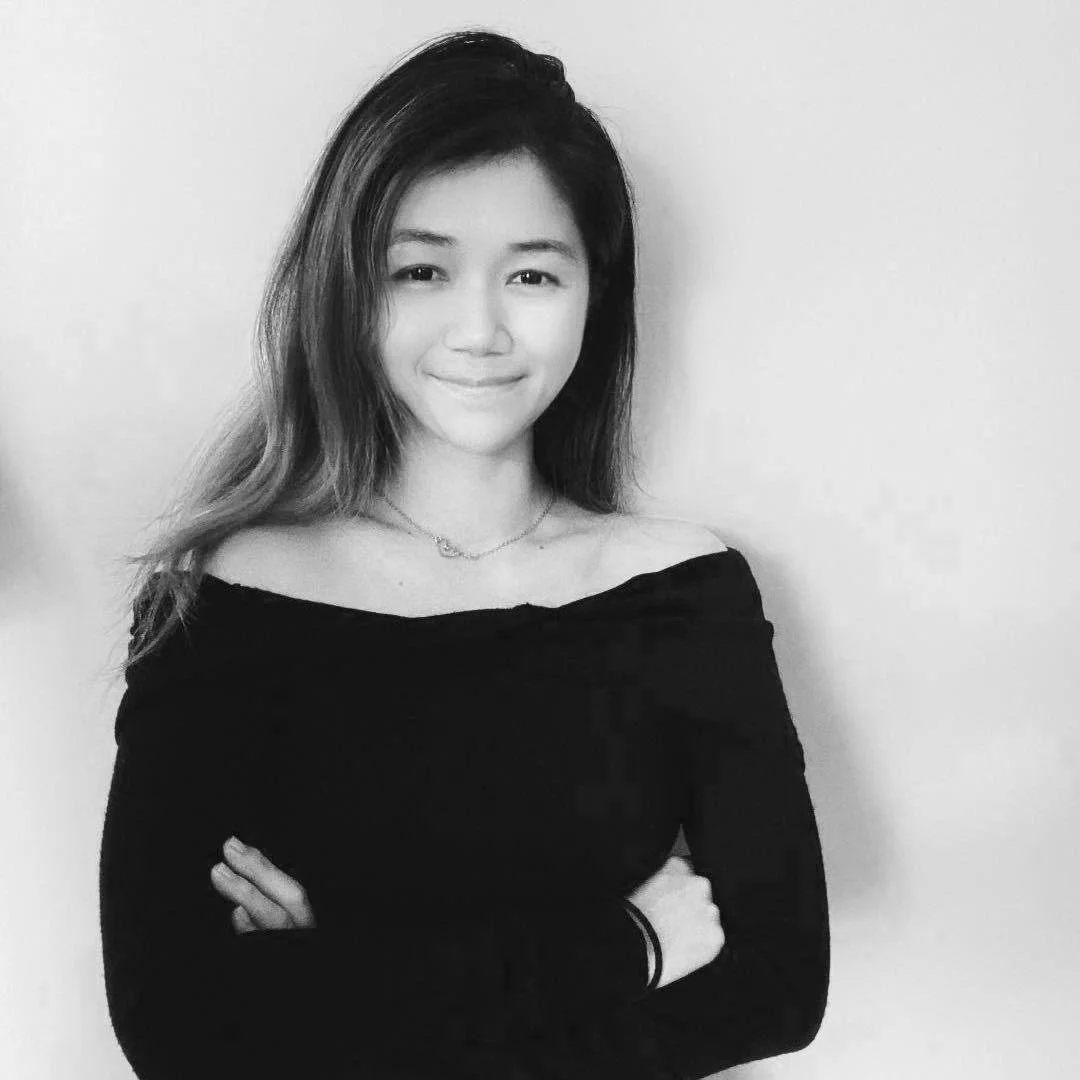 Black and white portrait of a woman with long hair, wearing a dark off-the-shoulder top, crossing her arms.