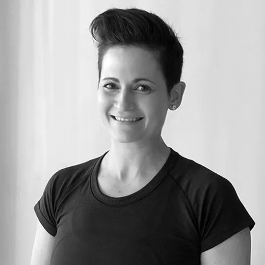 Person with short hair smiling and wearing a dark t-shirt, monochrome image.