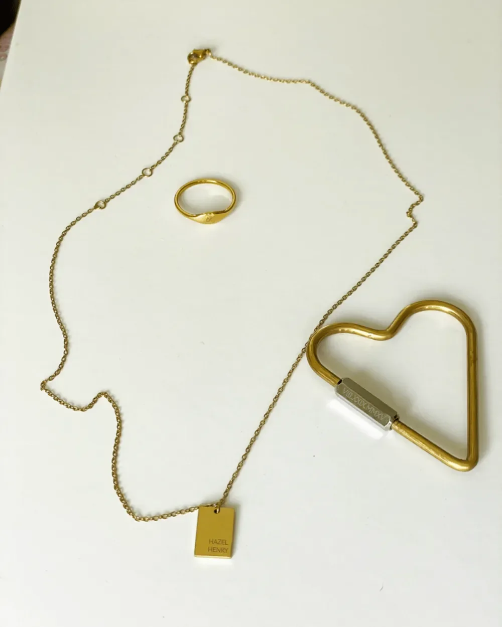 Engraved Mini Gold Tag necklace, engraved mini gold signet ring, engraved mixed metals heart carabiner keychain on white surface