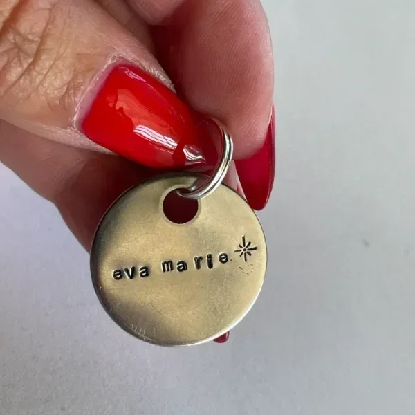 Close-up of hand holding a brass keychain tag hand-stamped with "eva marie" and a star icon in Sans Serif font