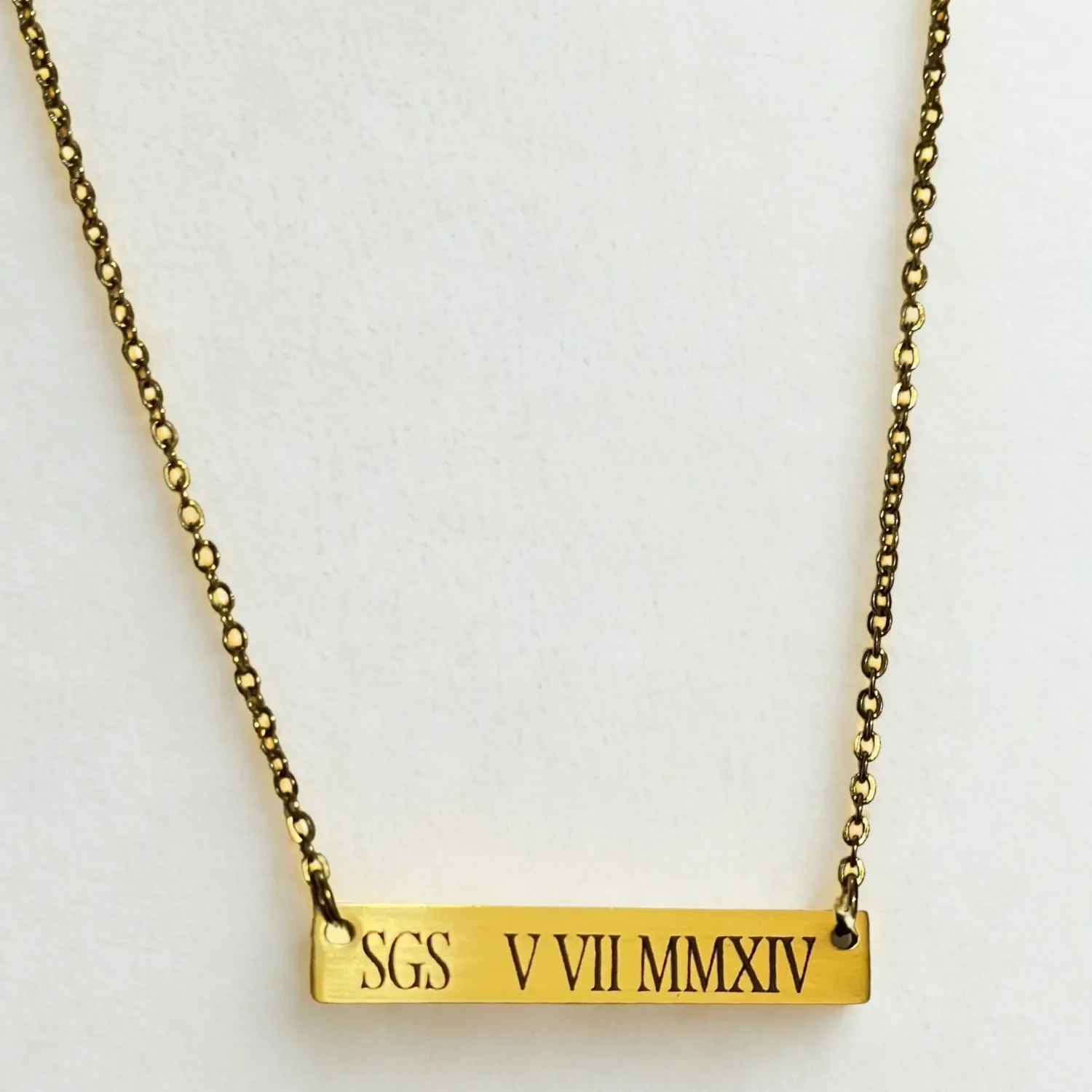 zClose-up of 14k gold plated personalized bar necklace engraved with Roman numerals on dainty gold chain, custom nameplate jewelry by Babe’s Hardware.