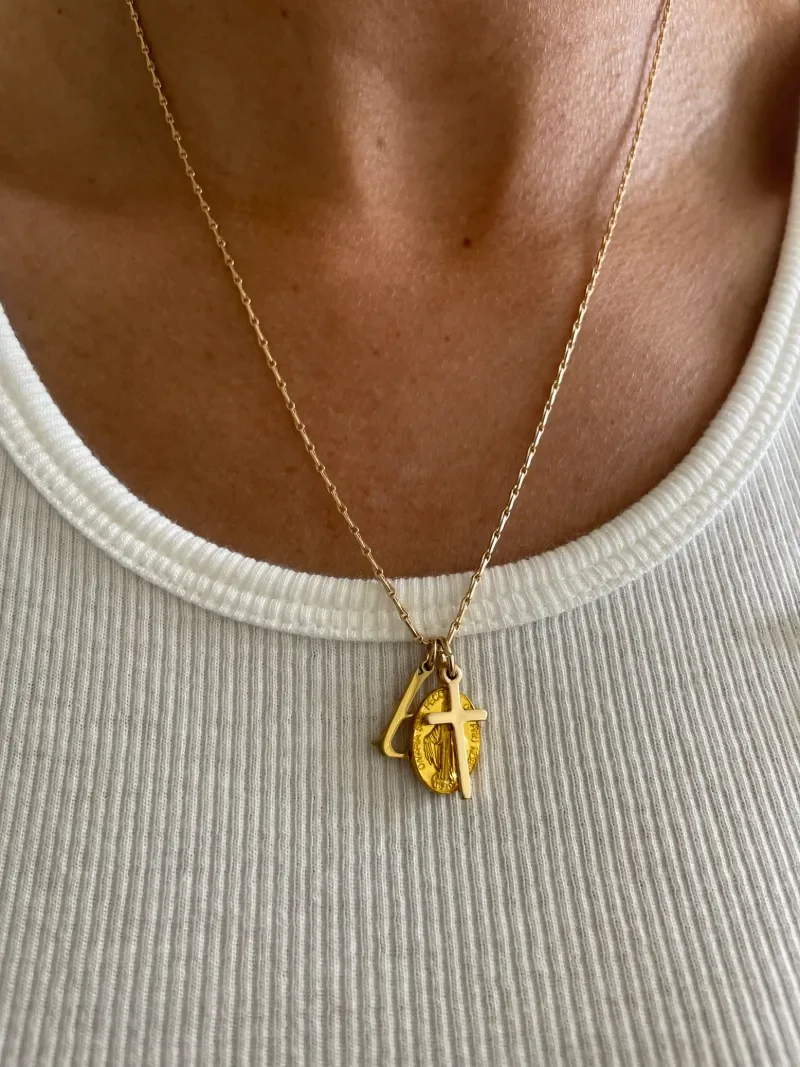 closeup of woman wearing gold necklace with gothic initial, Miraculous Medal pendant, and mini gold cross charm