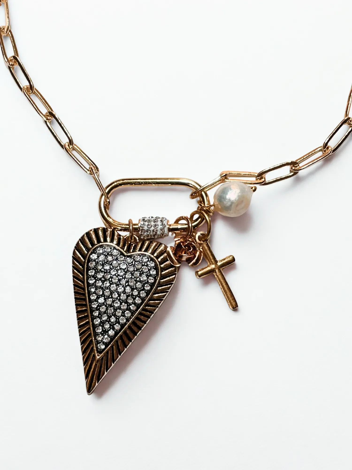 Close-up of 18k gold plated Pavé Heart Carabiner Necklace featuring a rhinestone-encrusted heart pendant with gold edging, pearl, rose, and mini cross charms.
