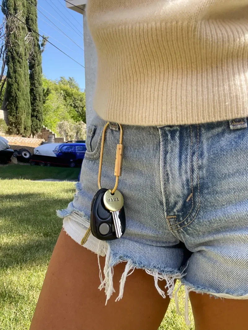 female outside with brass oval shape keychain with custom hand-stamped brass tag clipped onto her denim shorts