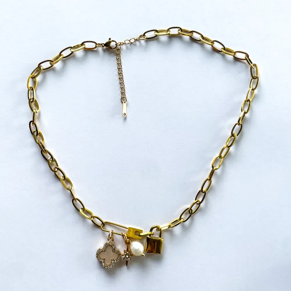 Gold charm necklace worn on black ribbed turtleneck showing locket, clover, pearl and starburst charms