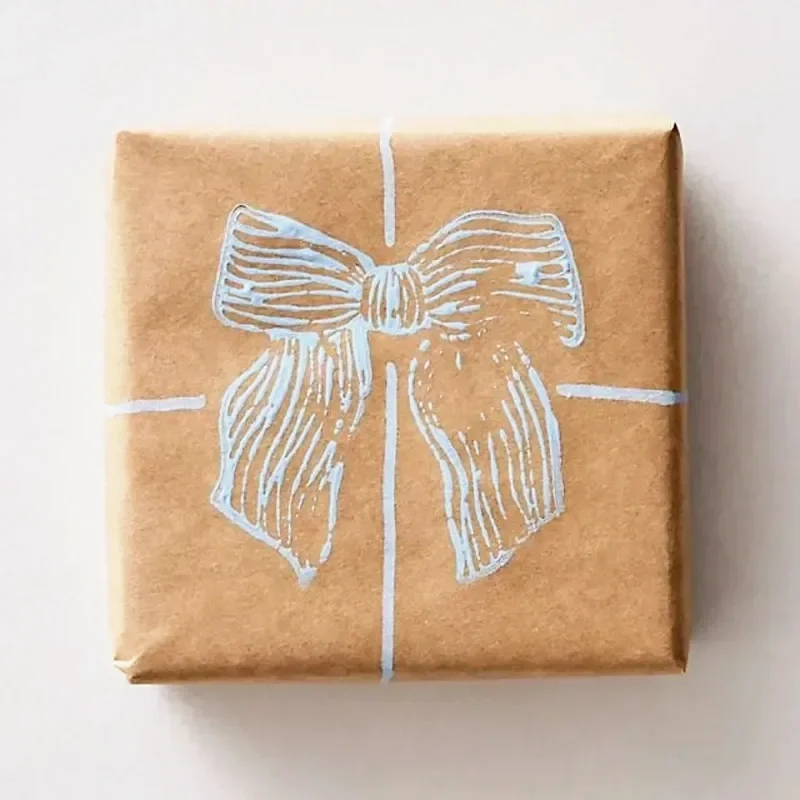 A small gift wrapped in brown paper with a white embroidery-style drawing of a bow on top.