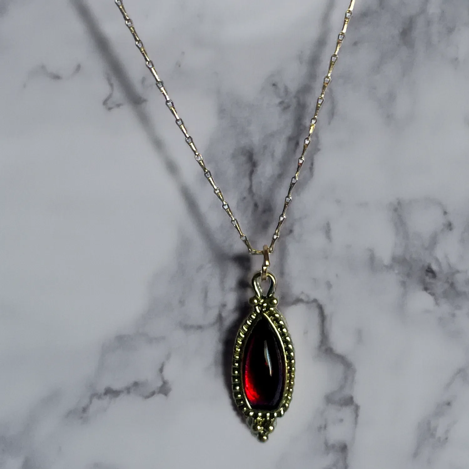 A delicate balance of vintage charm and understated elegance — featuring a deep red garnet drop pendant suspended from a fine gold-plated dog-bone chain.