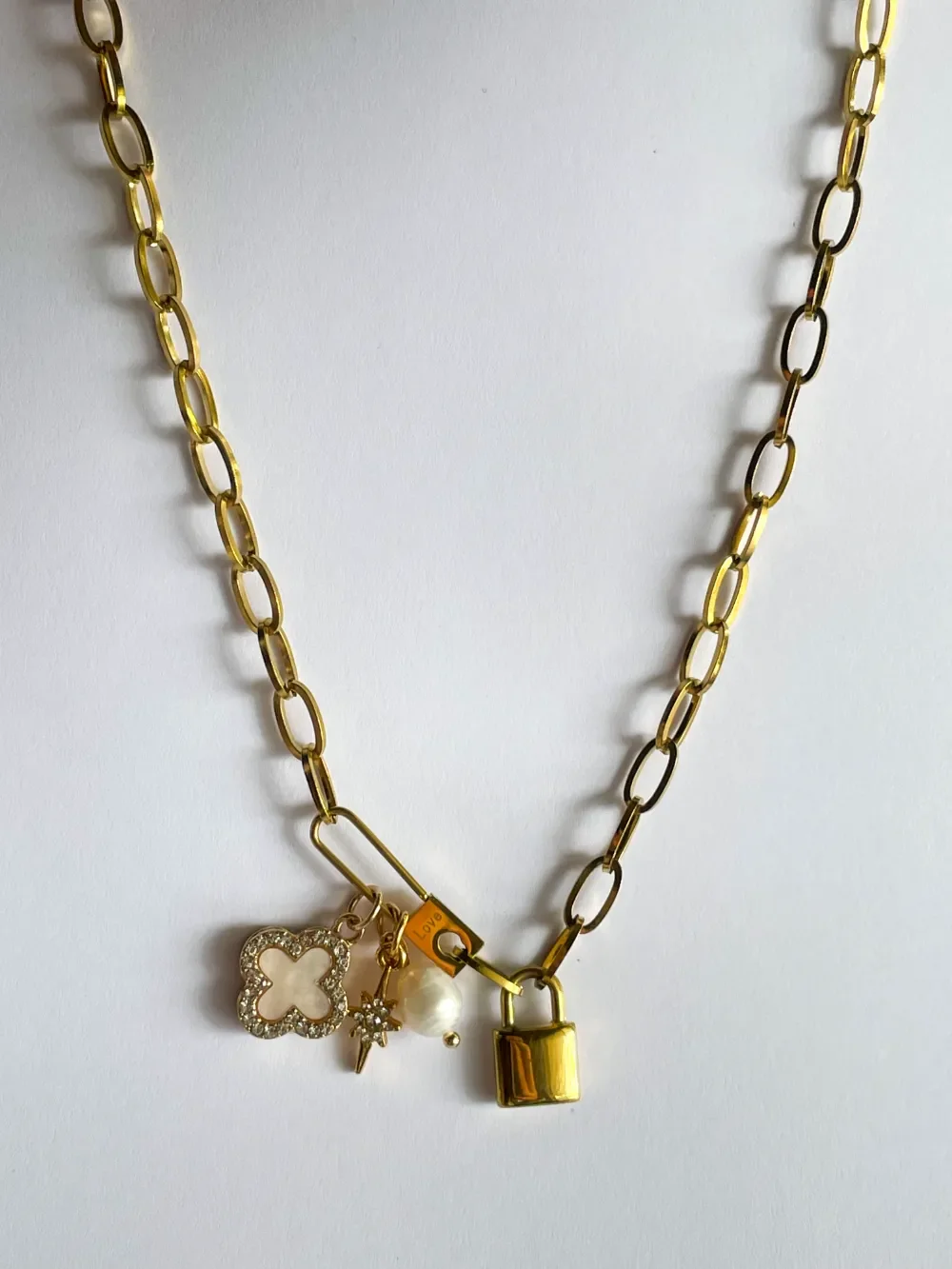 14k gold plated paperclip chain necklace with locket, pavé clover, starburst, and pearl charms laid flat on white background