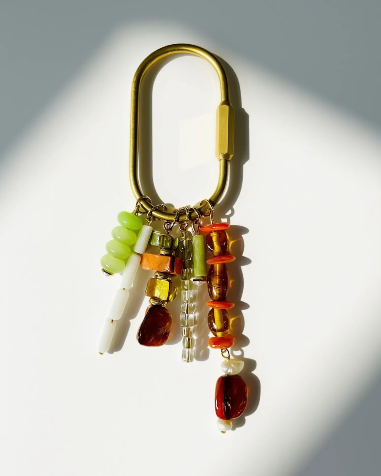 Close-up of the brass carabiner keychain charm showing amber, coral, mint, and pearl beaded strands.