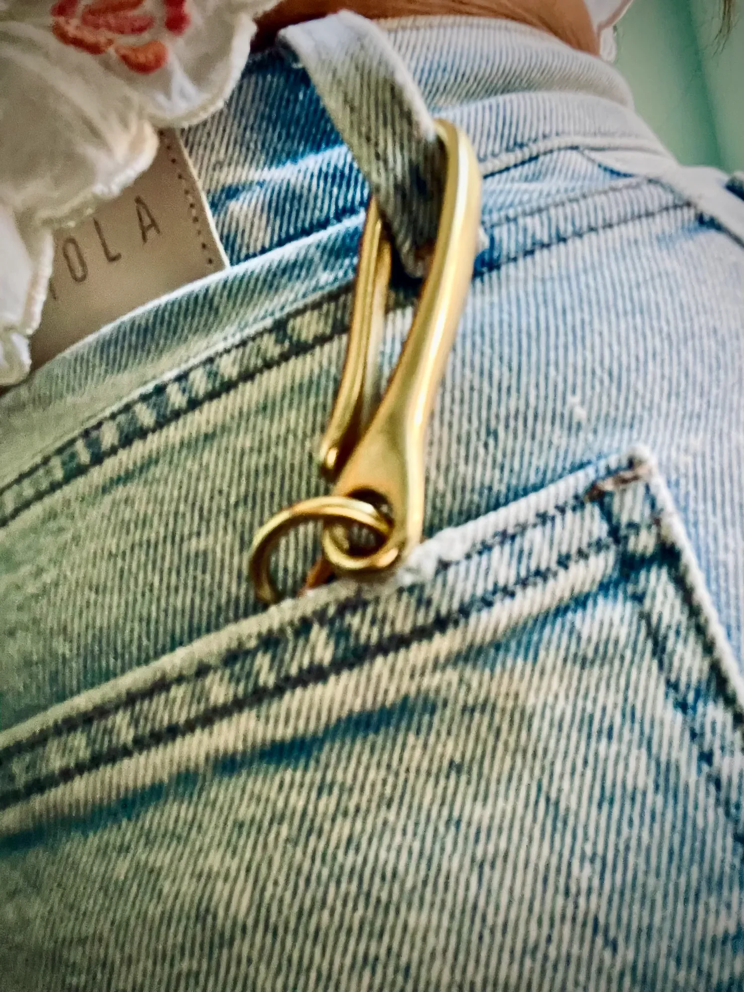Model wearing brass fish hook keychain hooked to denim shorts belt loop with keys attached