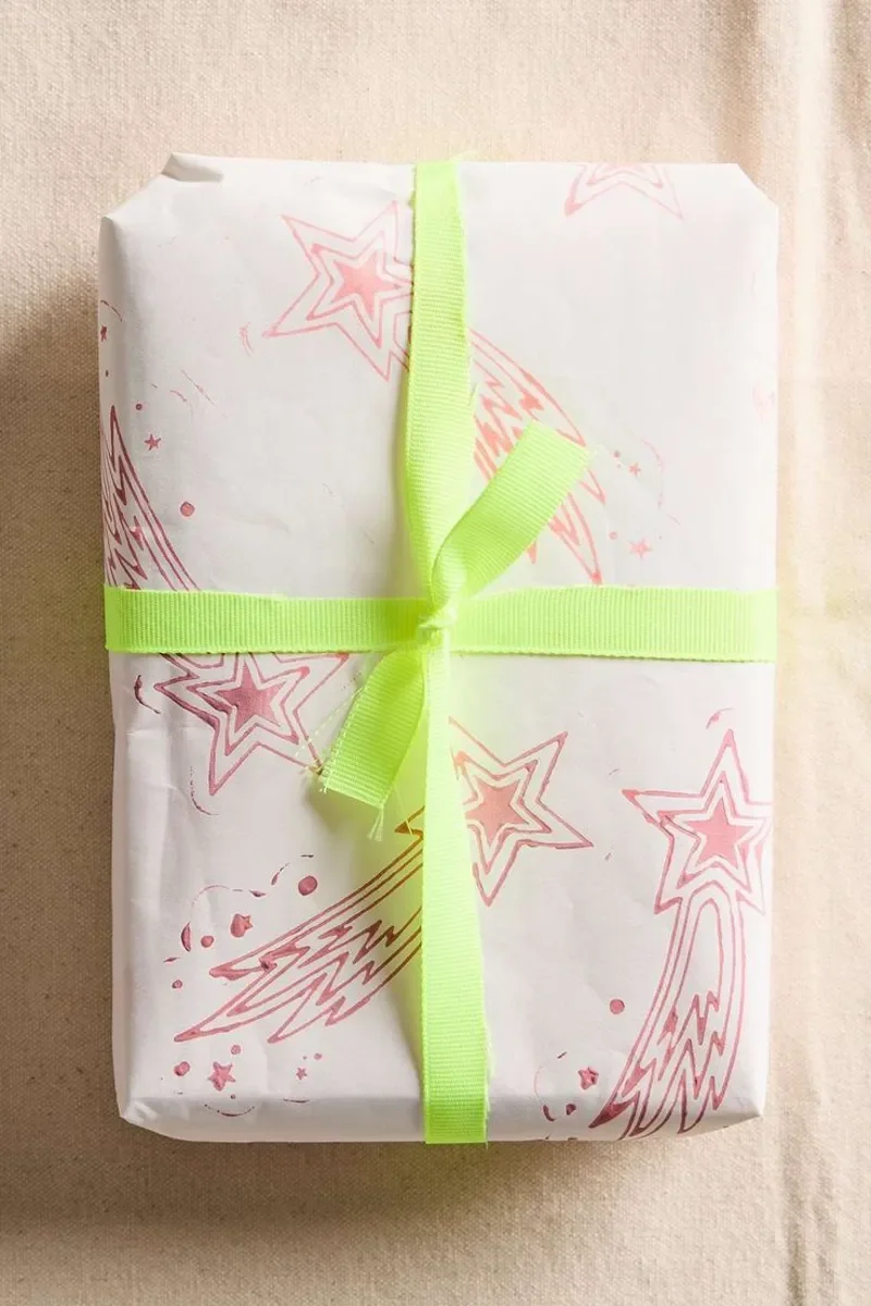 A gift wrapped in white paper with pink star and comet designs, tied with a bright yellow-green ribbon.
