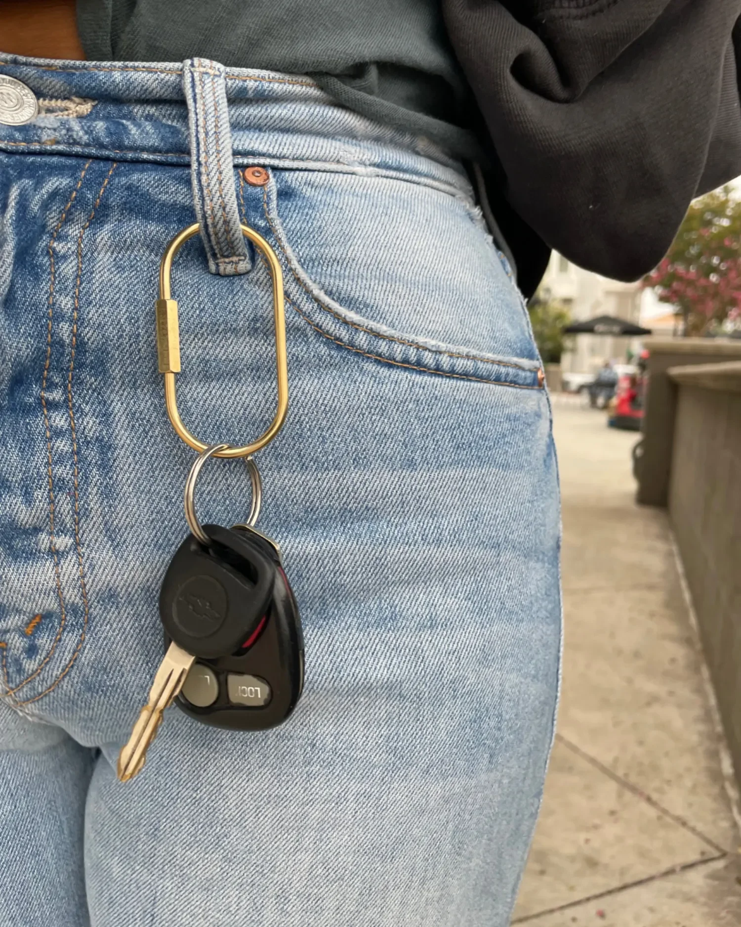 oval brass carabiner keychain attached to belt loop on womans jeans