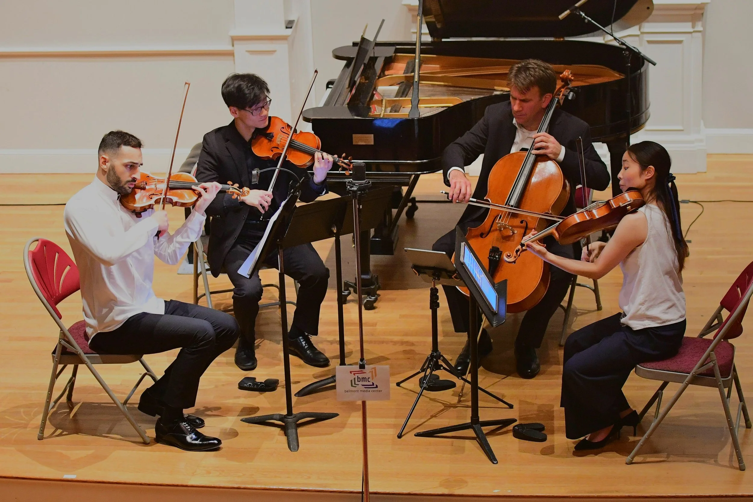 A classical music ensemble performing on stage, including two violinists, a cellist, and a pianist.