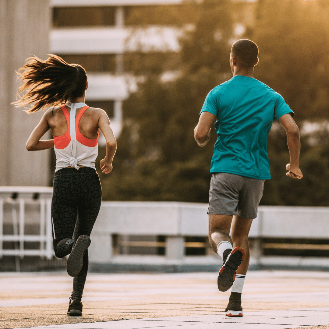 A man and a woman are running outdoors during sunset, wearing athletic clothing.