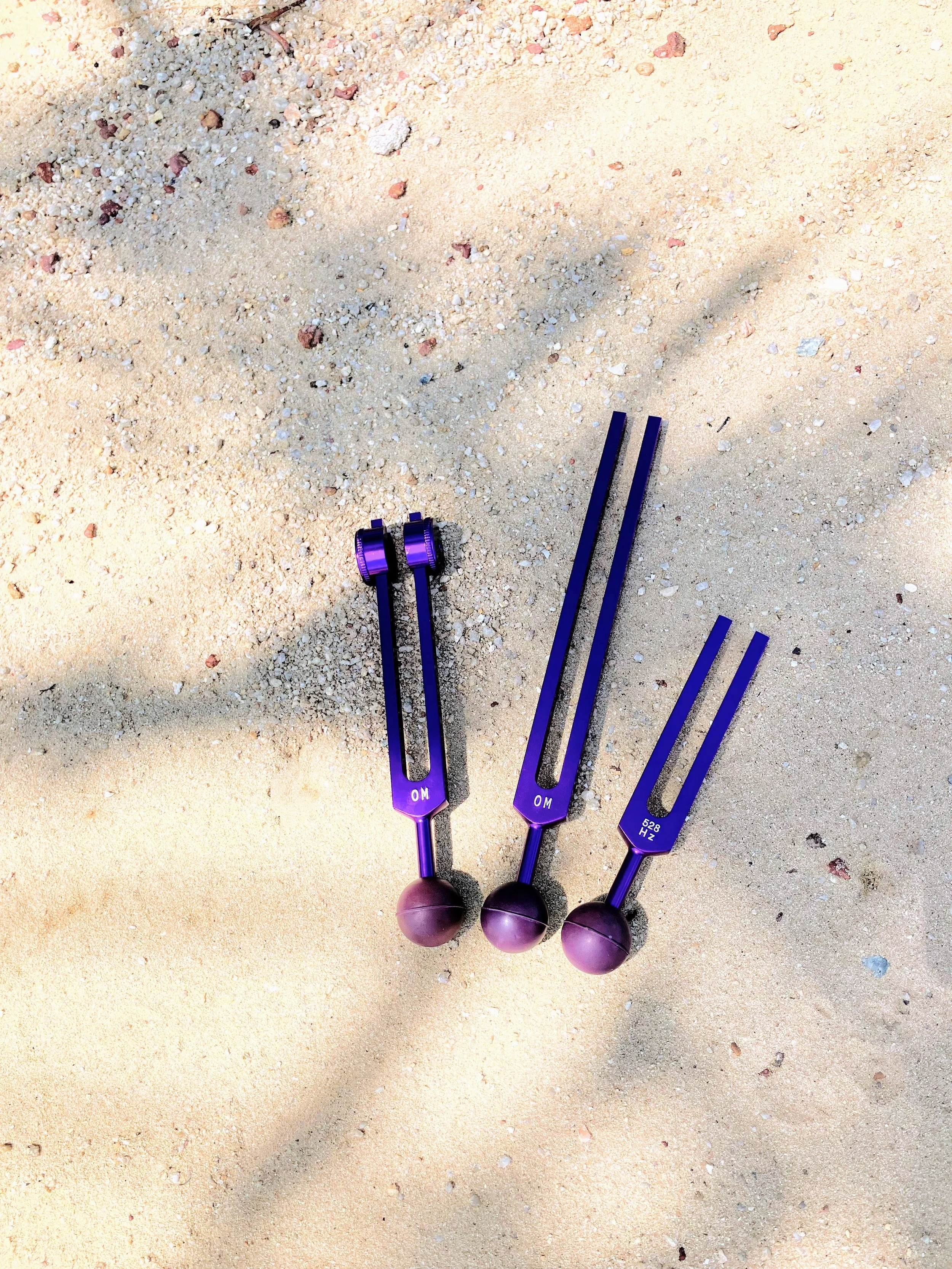 Three purple tuning forks with ball-ended tools on sandy ground.