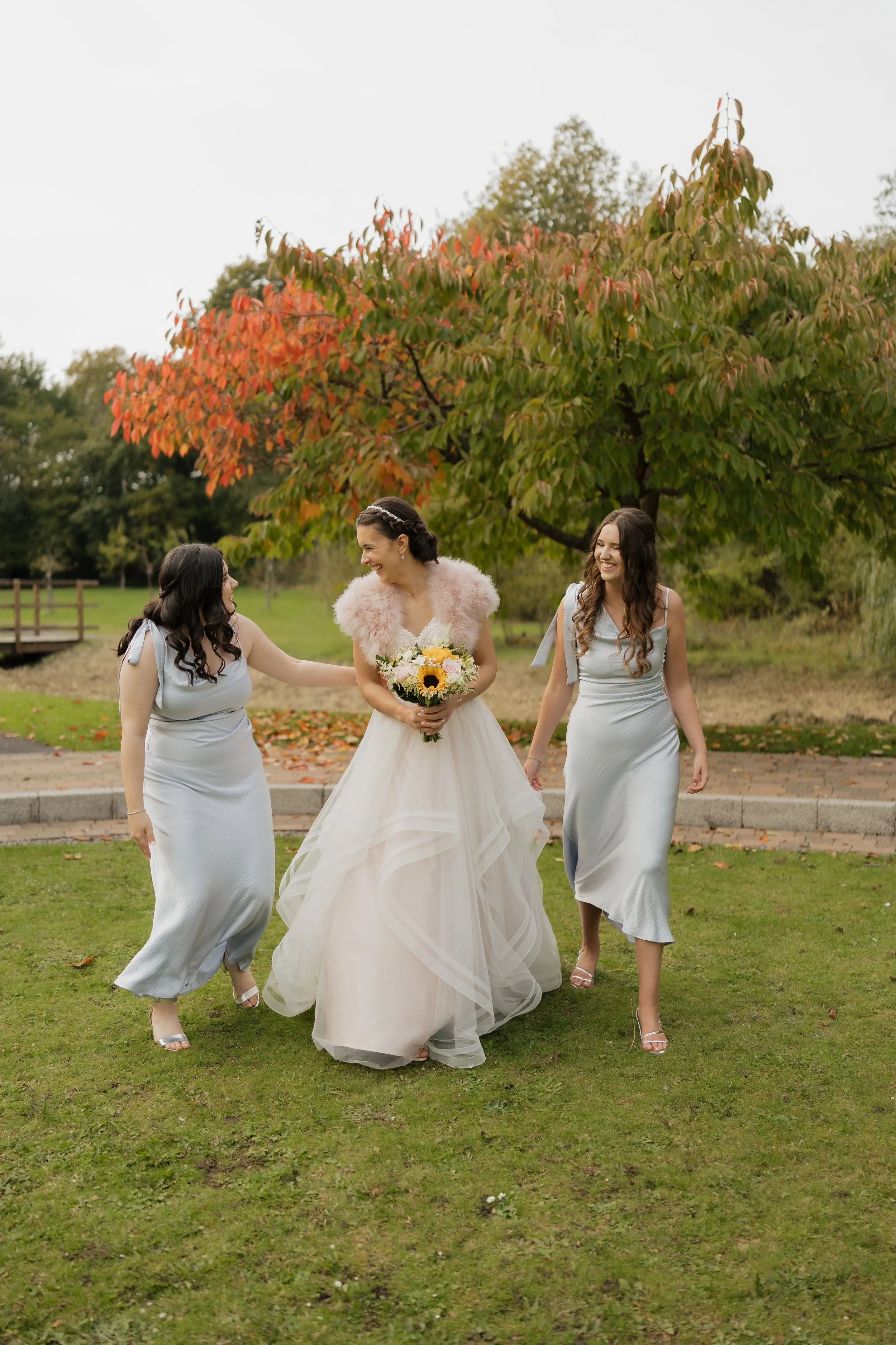 Brunette bride with red hair in a white wedding dress and veil outdoors, smiling at camera with trees and grass in the background.