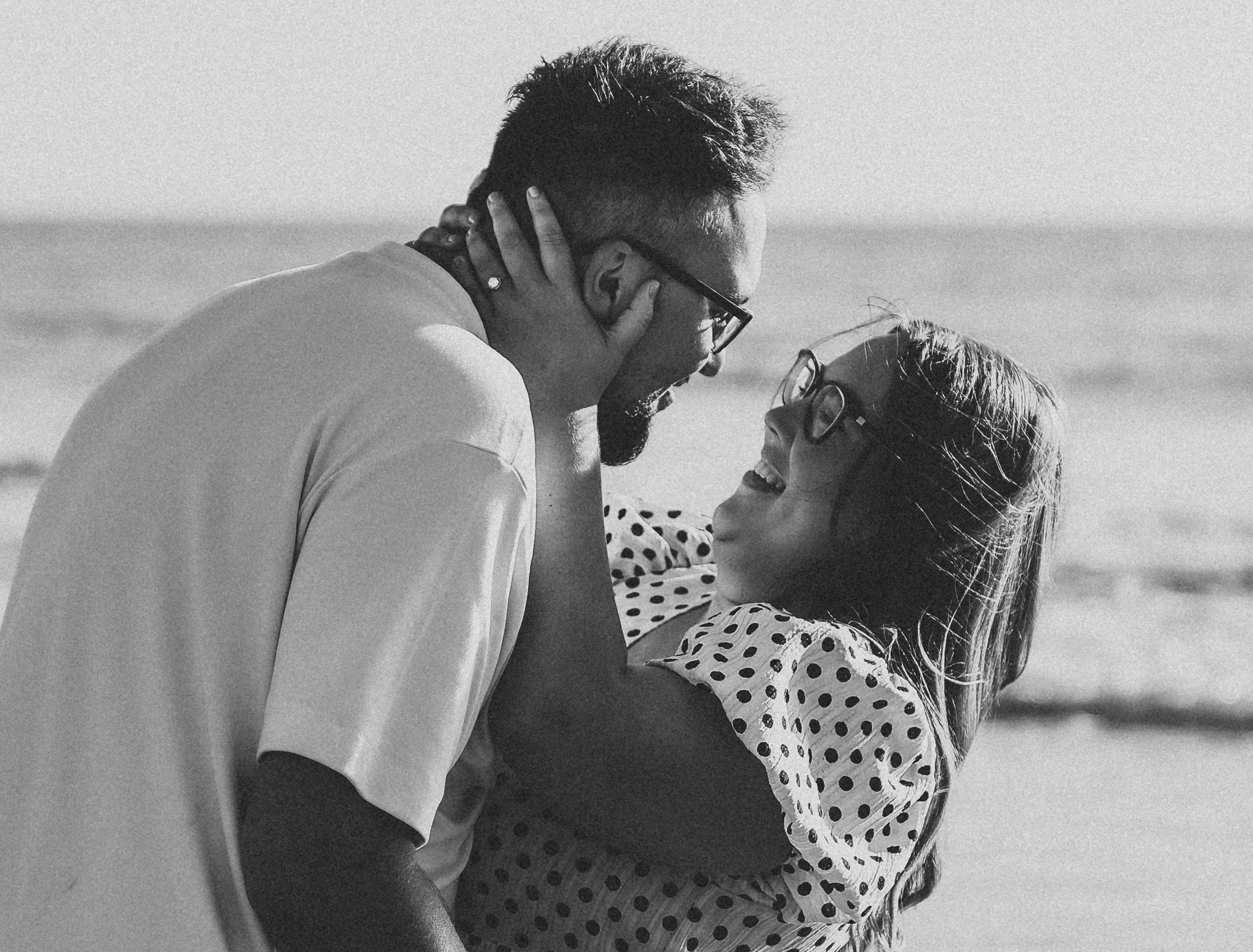 Couple embracing and laughing on a beach in black and white.
