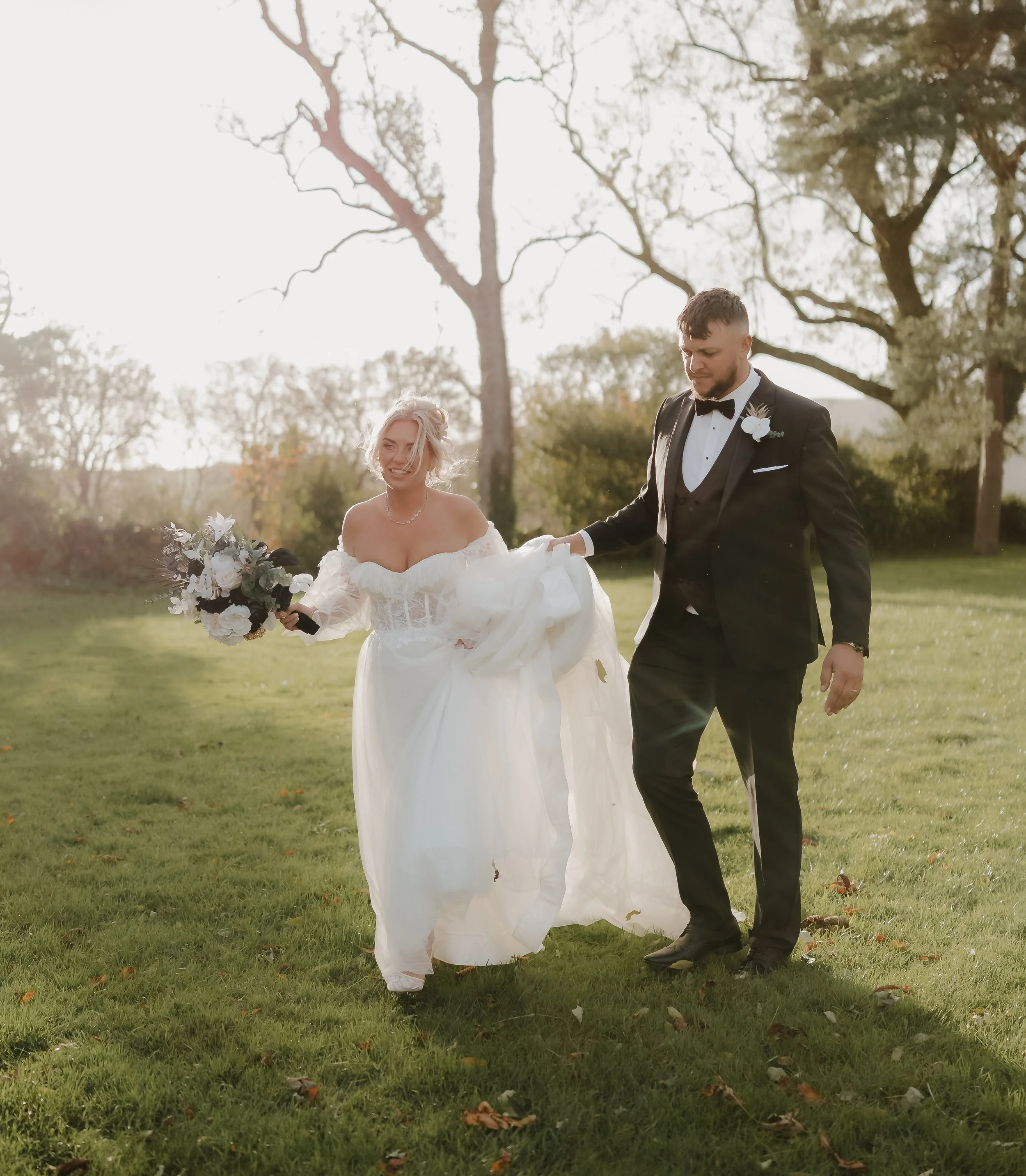 Bride and groom holding hands in a garden, walking on a stone path.
