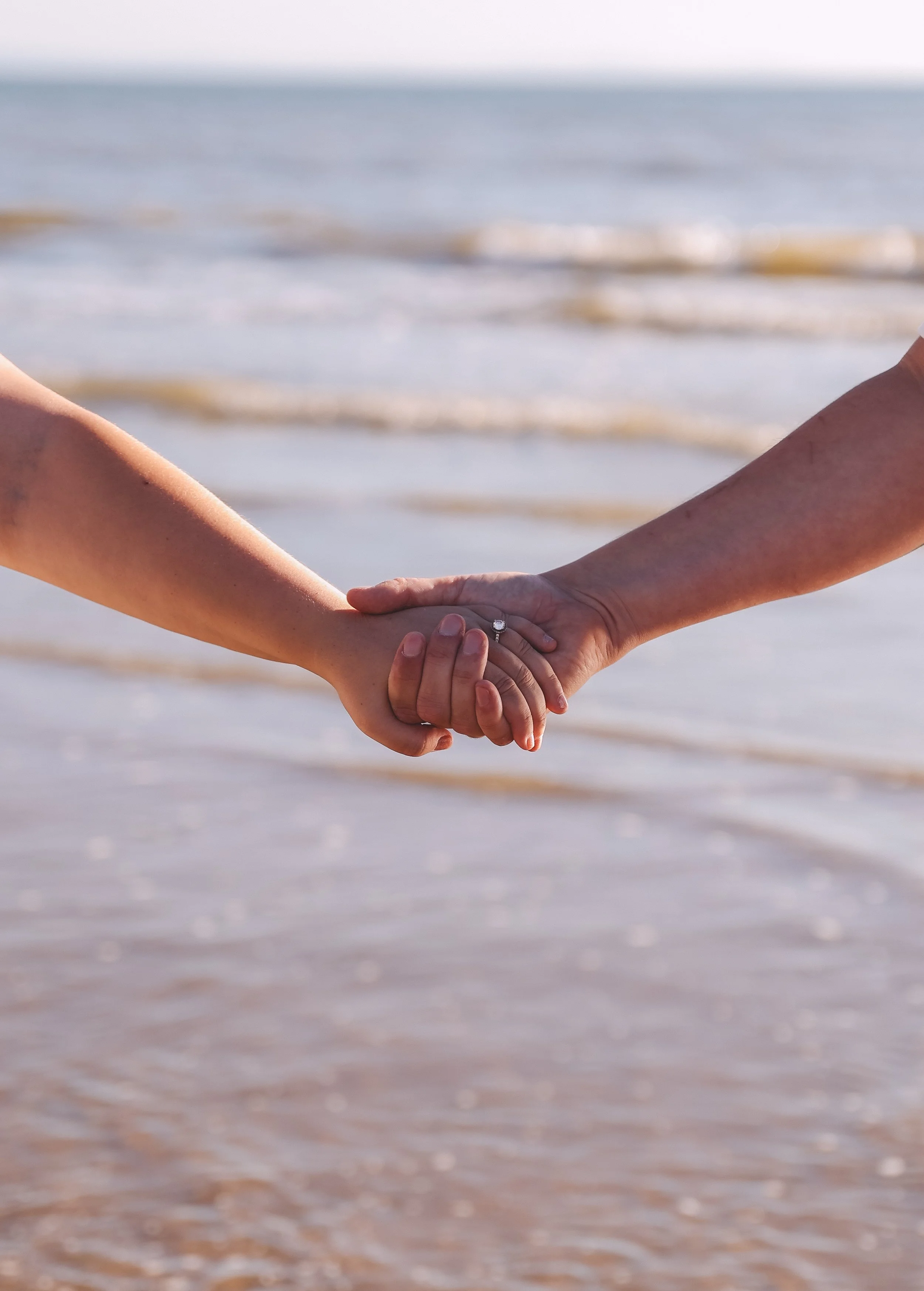 Two people holding hands with a beach in the background.